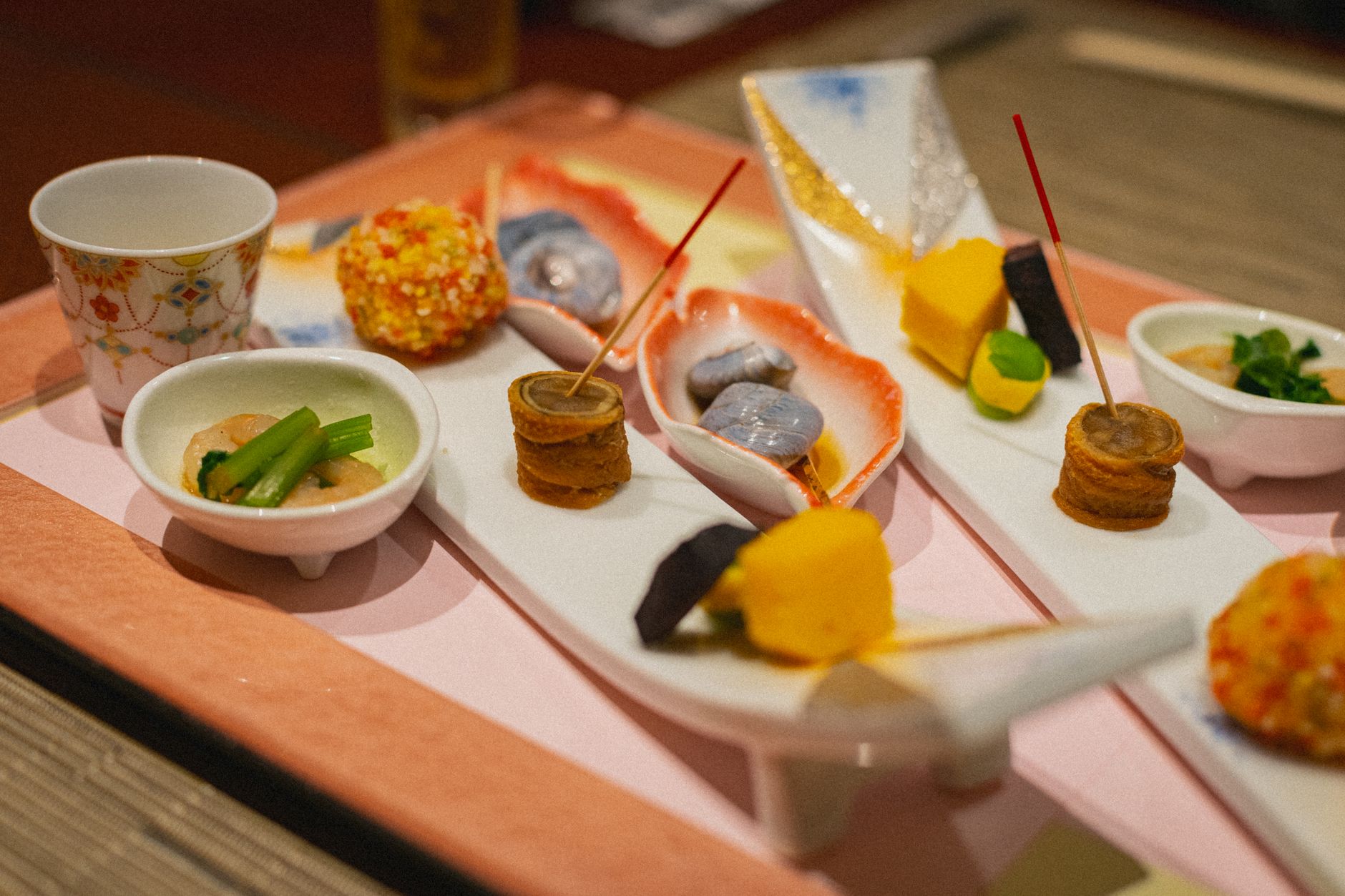 A tray of small Japanese kaiseki dishes with skewered bites and lacquered bowls