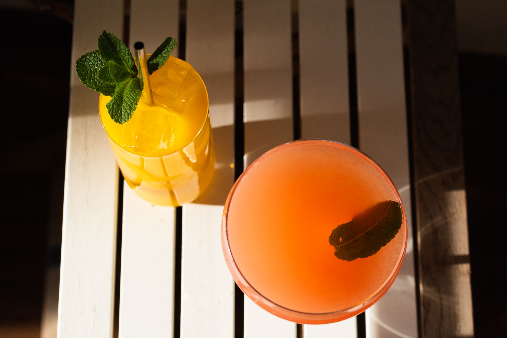 Two citrus and mint drinks photographed from above on a white slatted table in sunlight