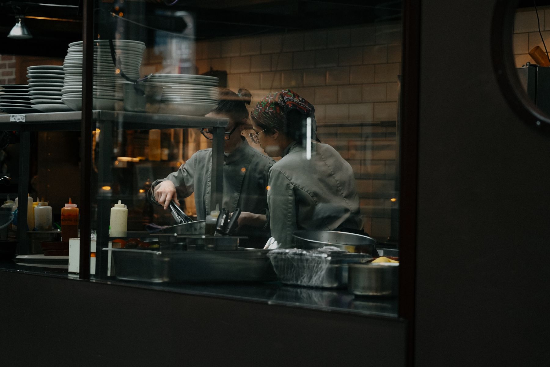 Zwei Köche richten gemeinsam Teller an, gesehen durch das Passfenster einer Restaurantküche