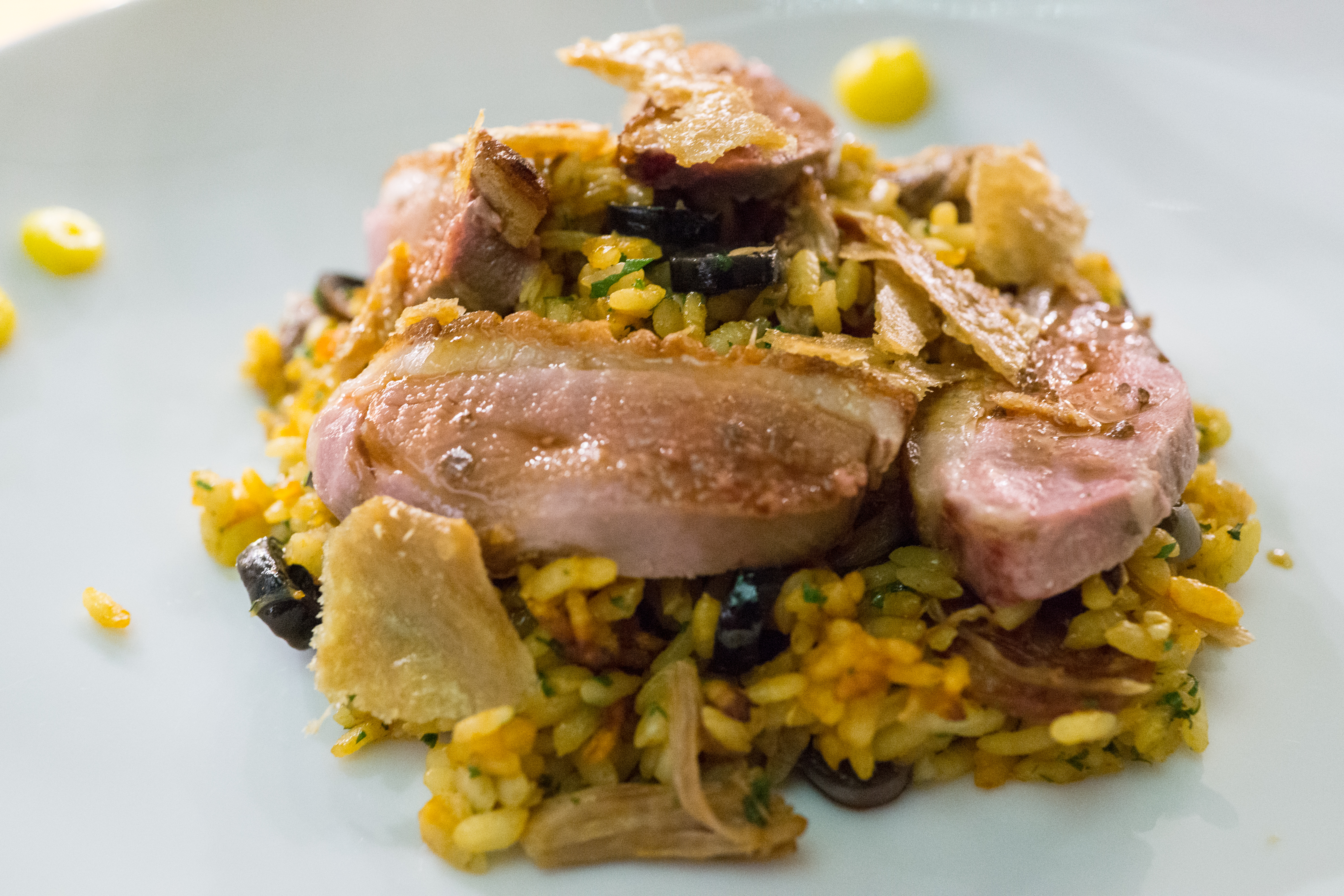 Sliced duck breast on golden rice with crisp crackling and black olives