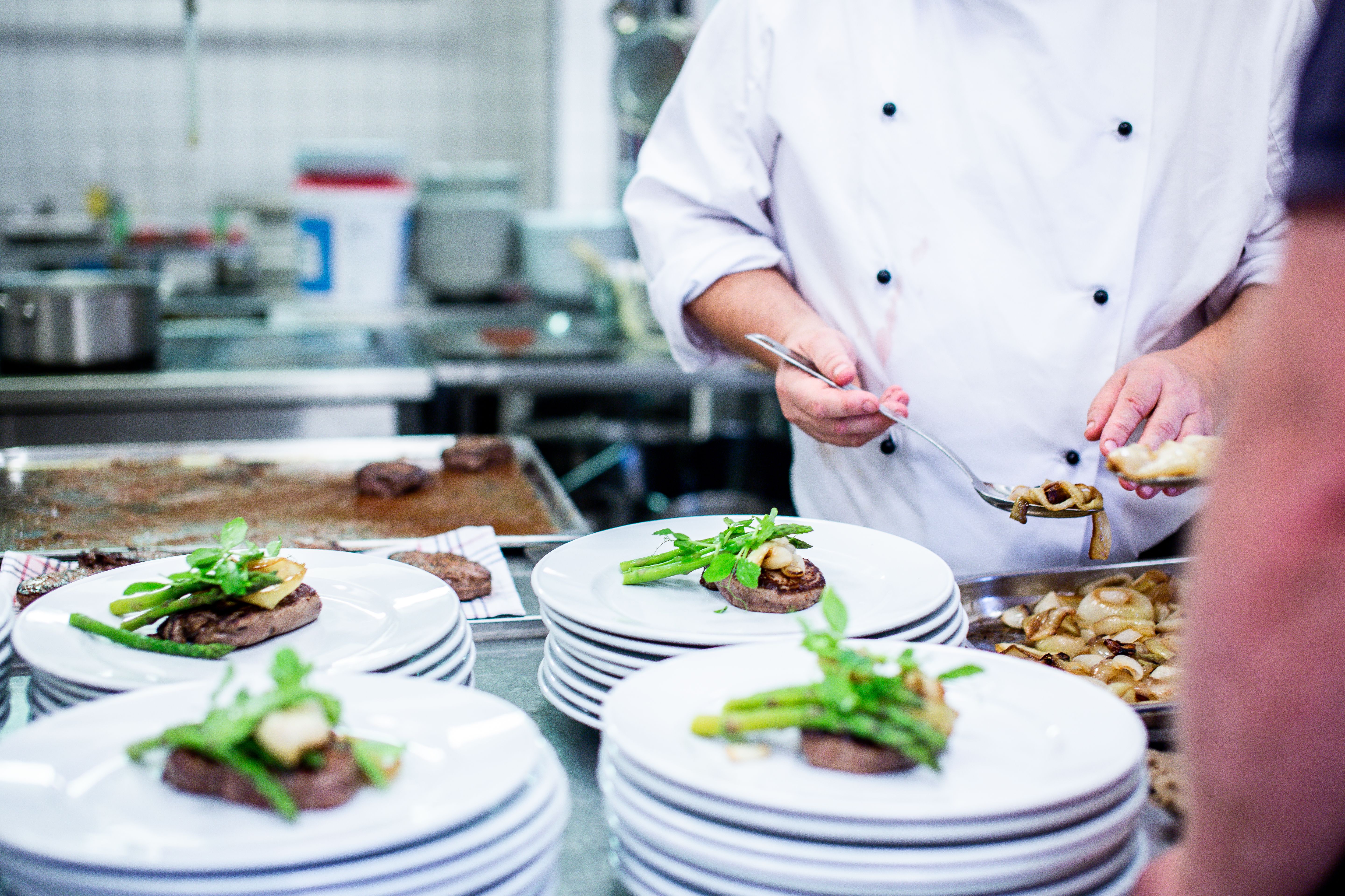 Chef impiatta manzo scottato con asparagi su piatti bianchi in una cucina professionale