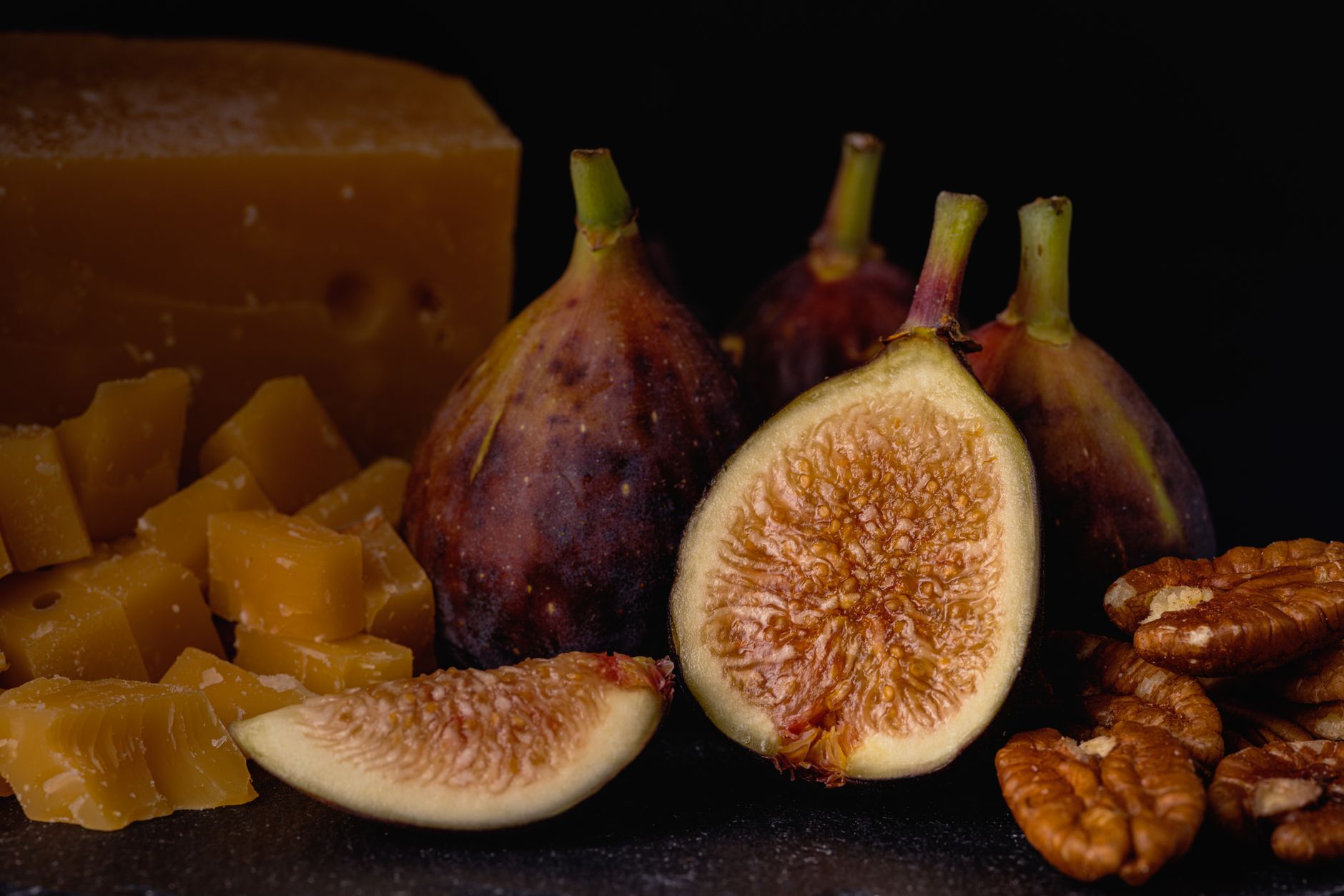 Whole and halved ripe figs beside a block of cheese and shelled pistachios