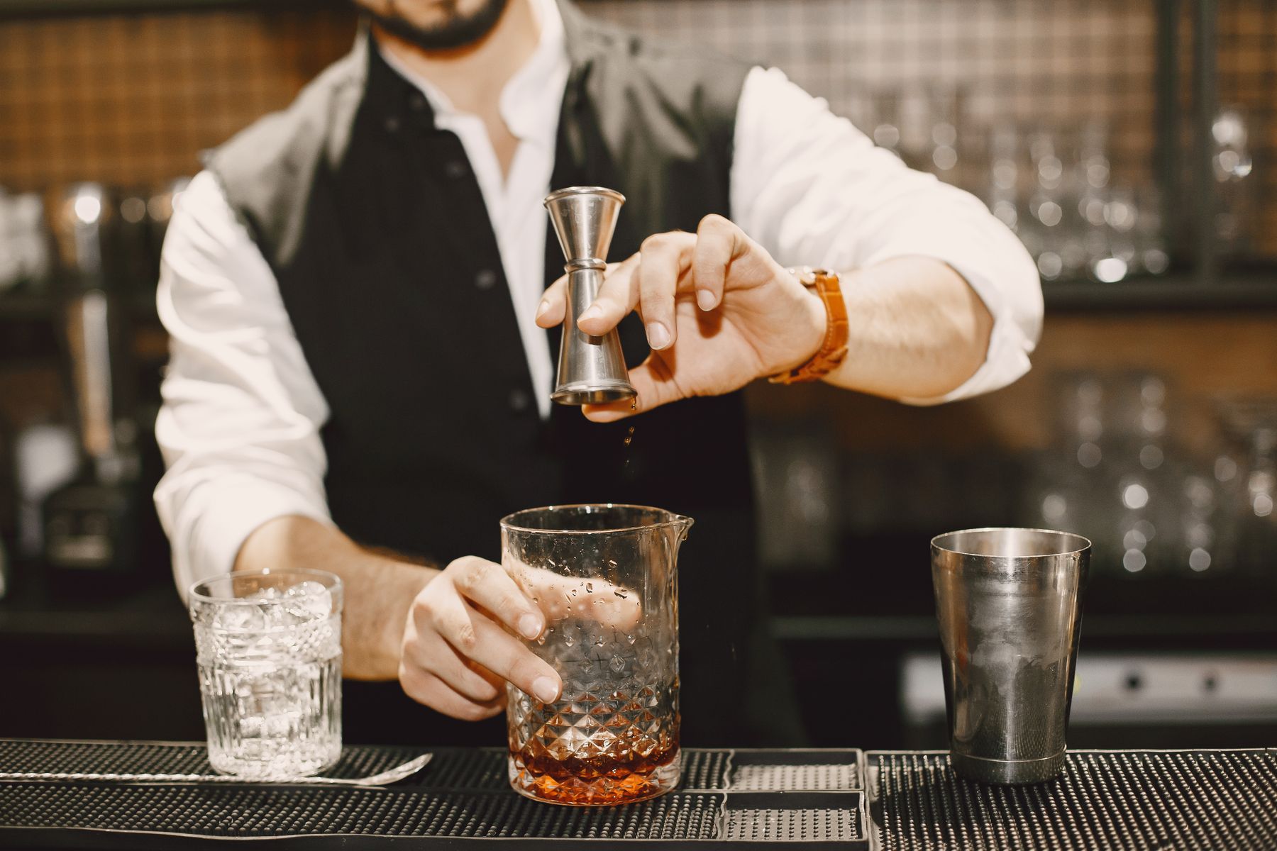 A bartender measuring spirits with a jigger while mixing a cocktail