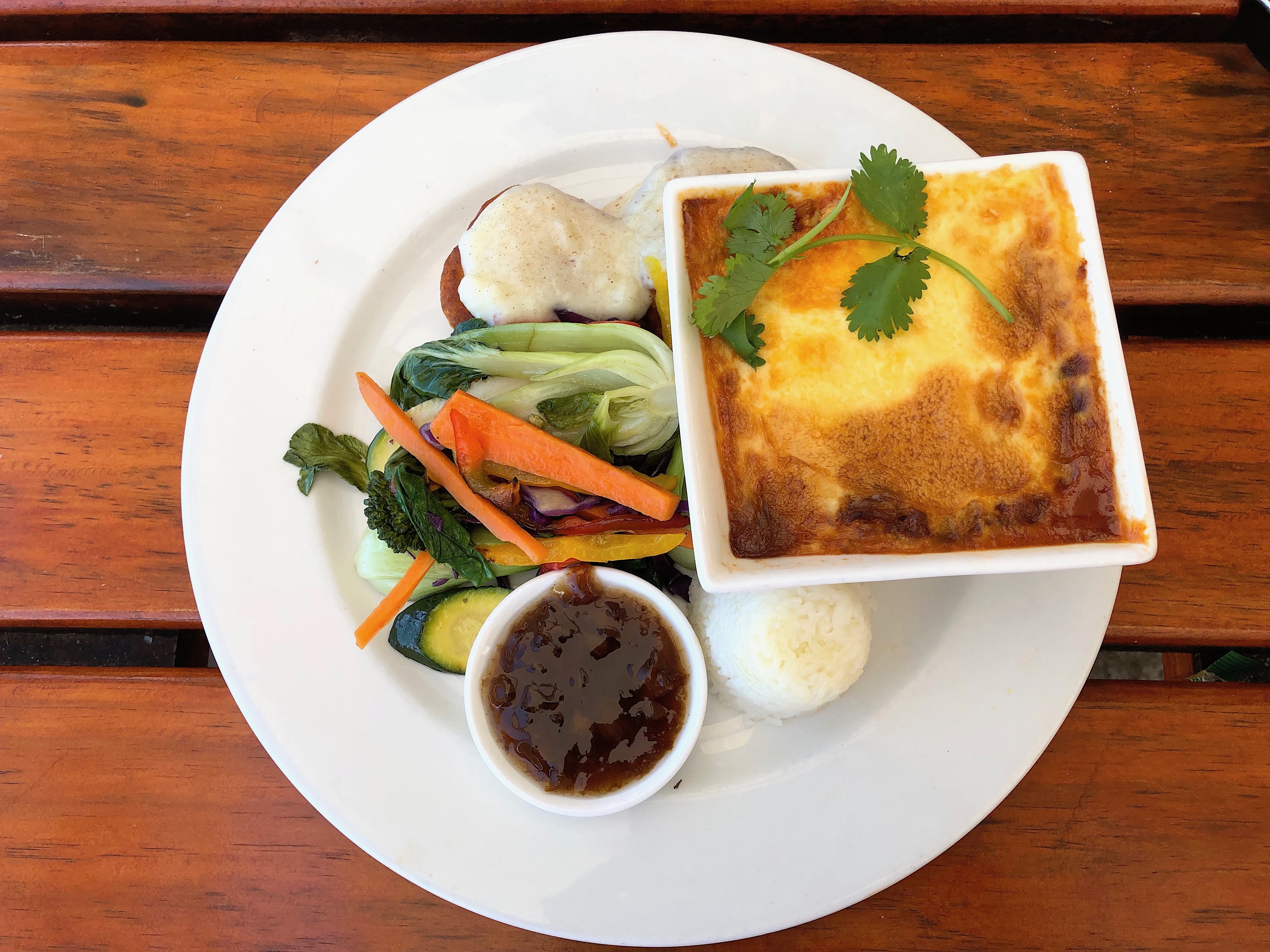 Baked bobotie in a square dish with golden egg topping, coriander, rice and chutney