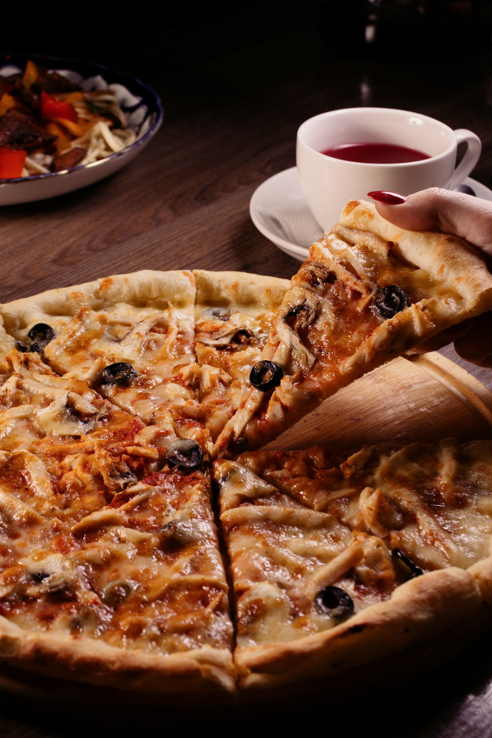 A hand lifting a cheese and olive pizza slice at a casual dining restaurant table
