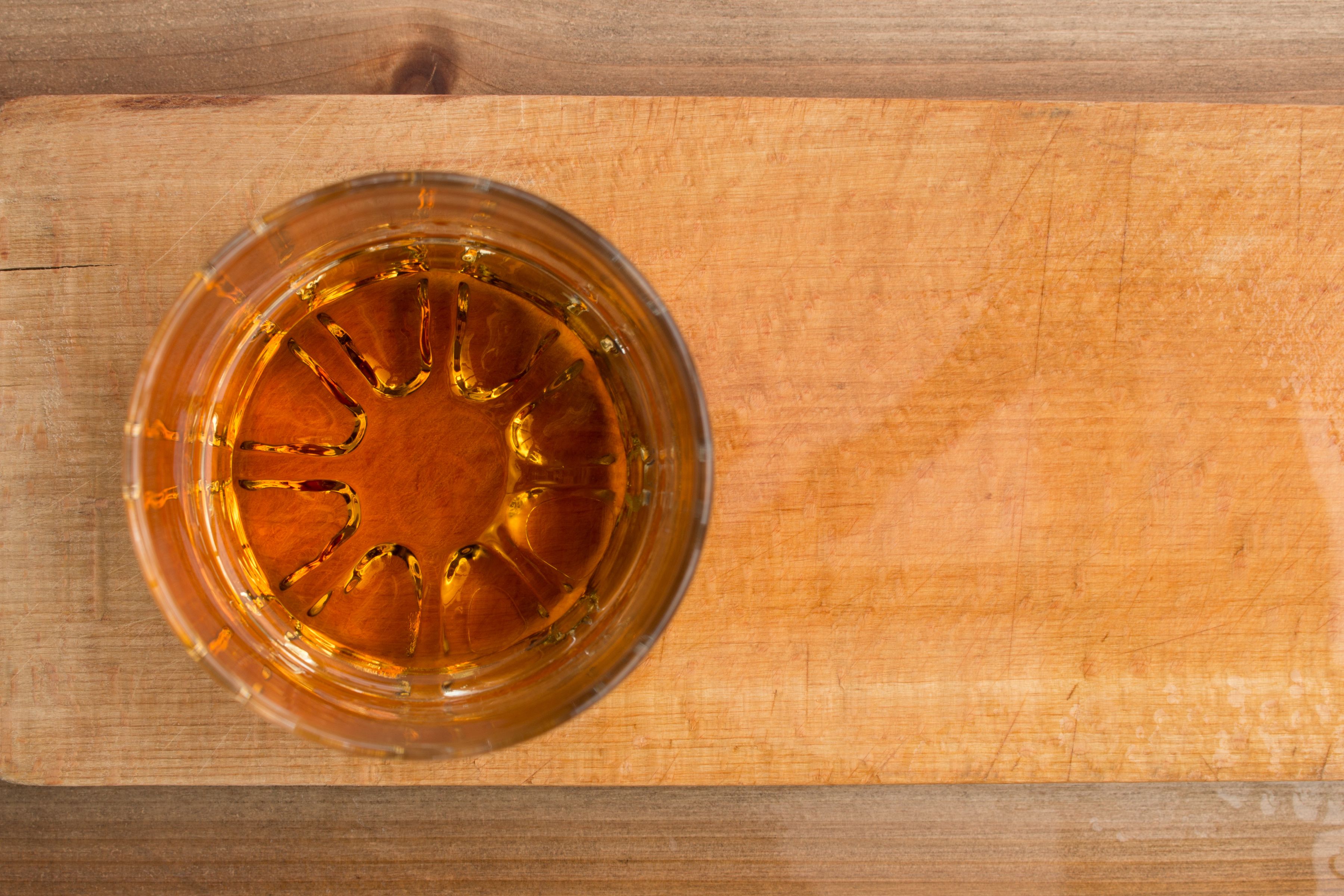 Overhead view of a glass of amber bourbon whiskey on a wooden board