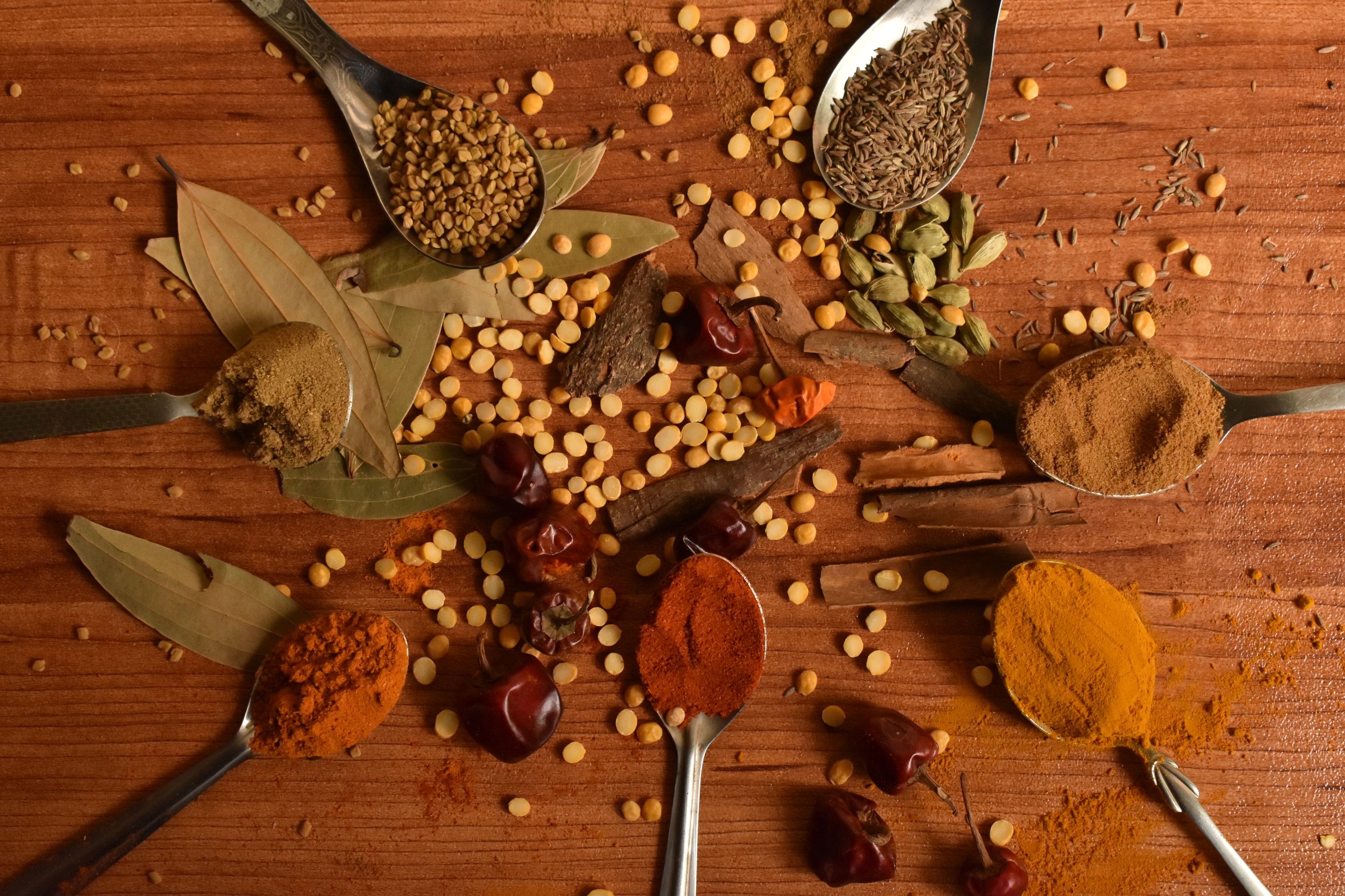 An overhead spread of colourful Indian spices, chillies and cinnamon on wooden spoons