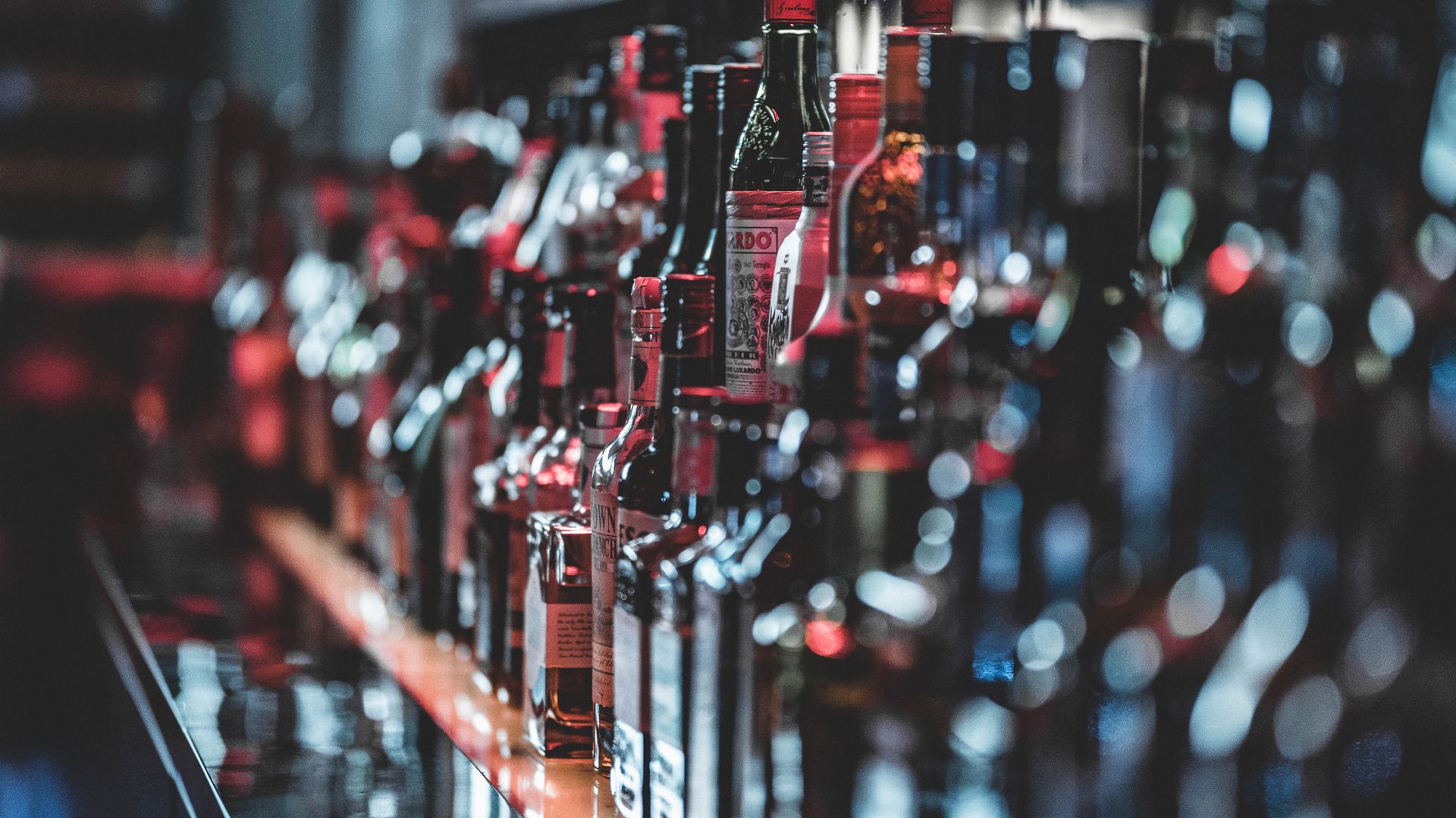 Row of spirits bottles on a lit bar shelf, most of them out of focus