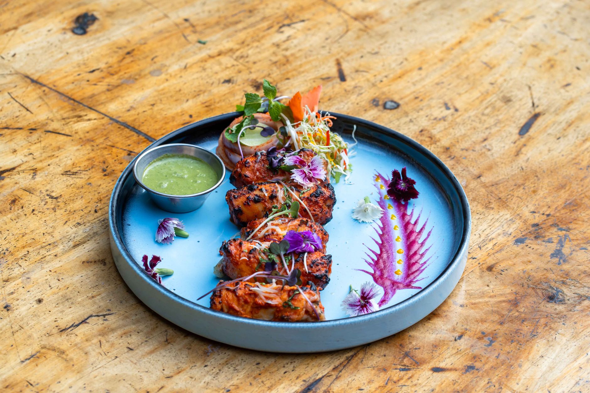 A plate of charred tandoori seafood skewers with mint chutney and edible flowers