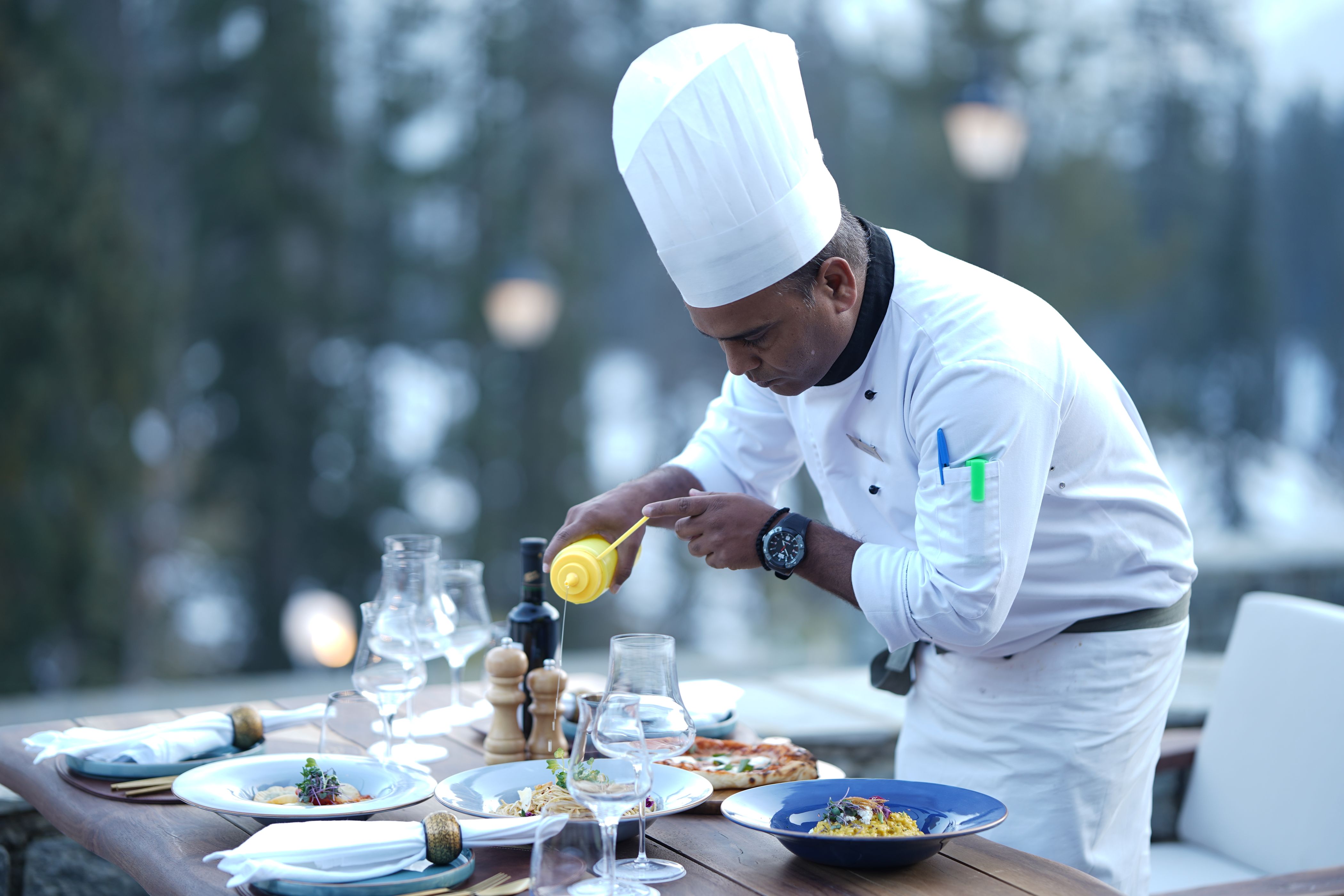 Chef con toque bianco che rifinisce i piatti a un tavolo di ristorante all'aperto in montagna