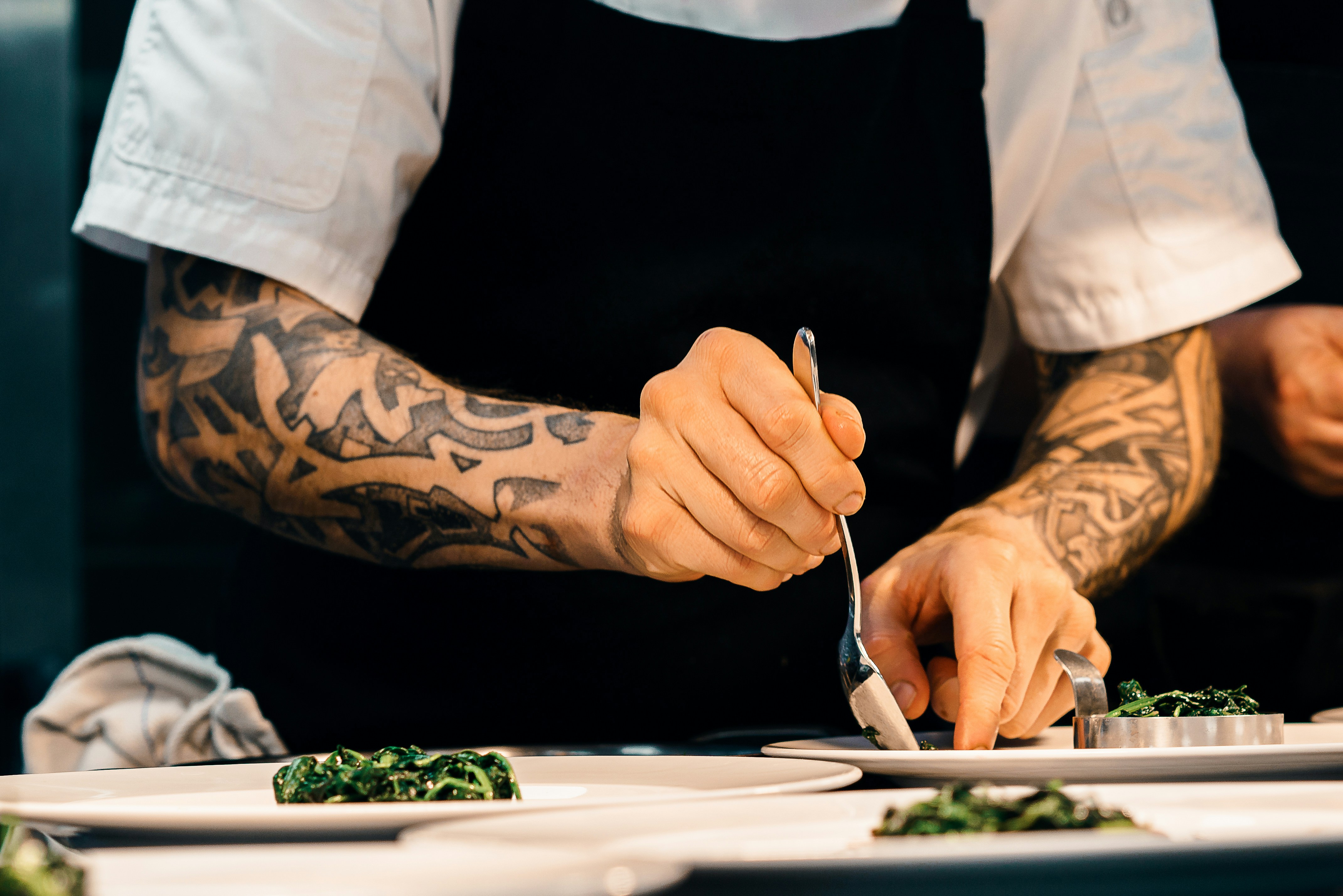 Un chef tatuado emplatando un plato de verduras salteadas en una cocina de restaurante