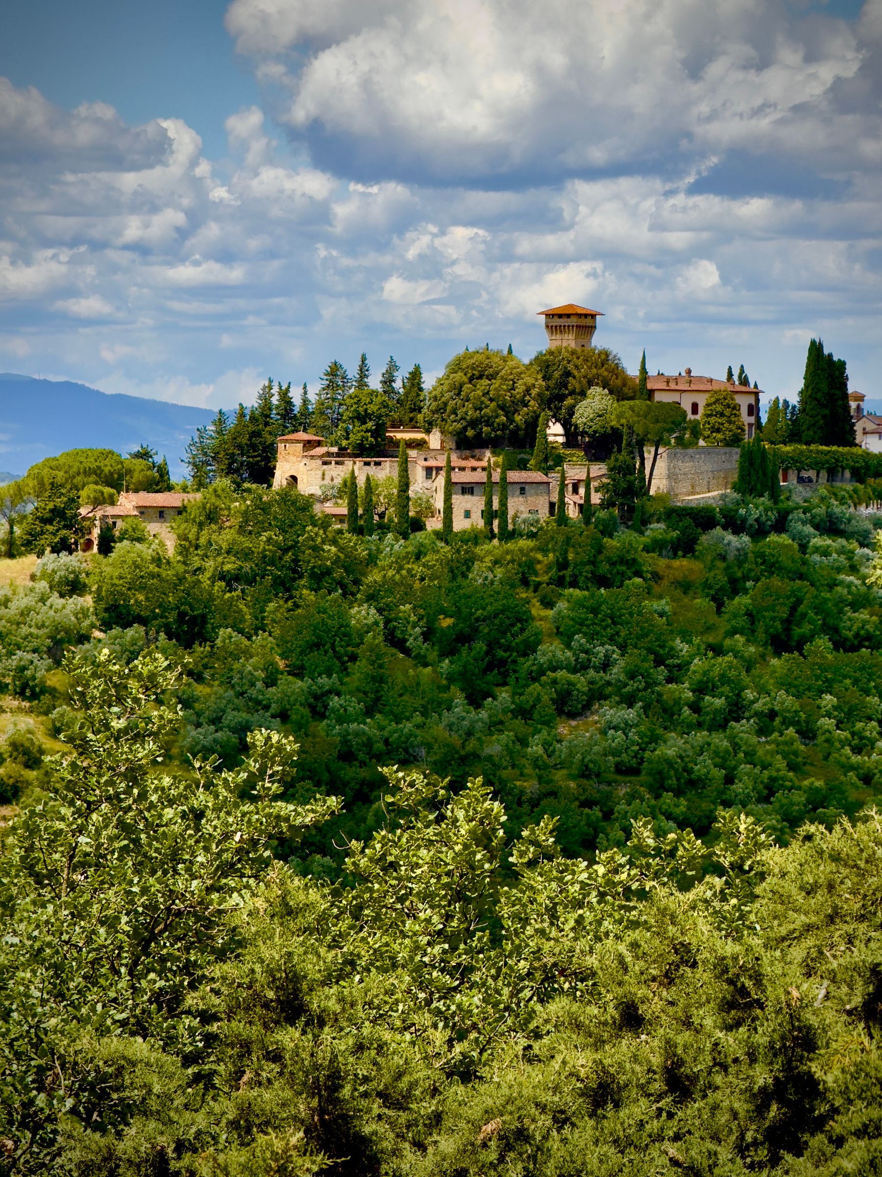 Hilltop stone village with a tower surrounded by vineyards and cypress trees in Chianti