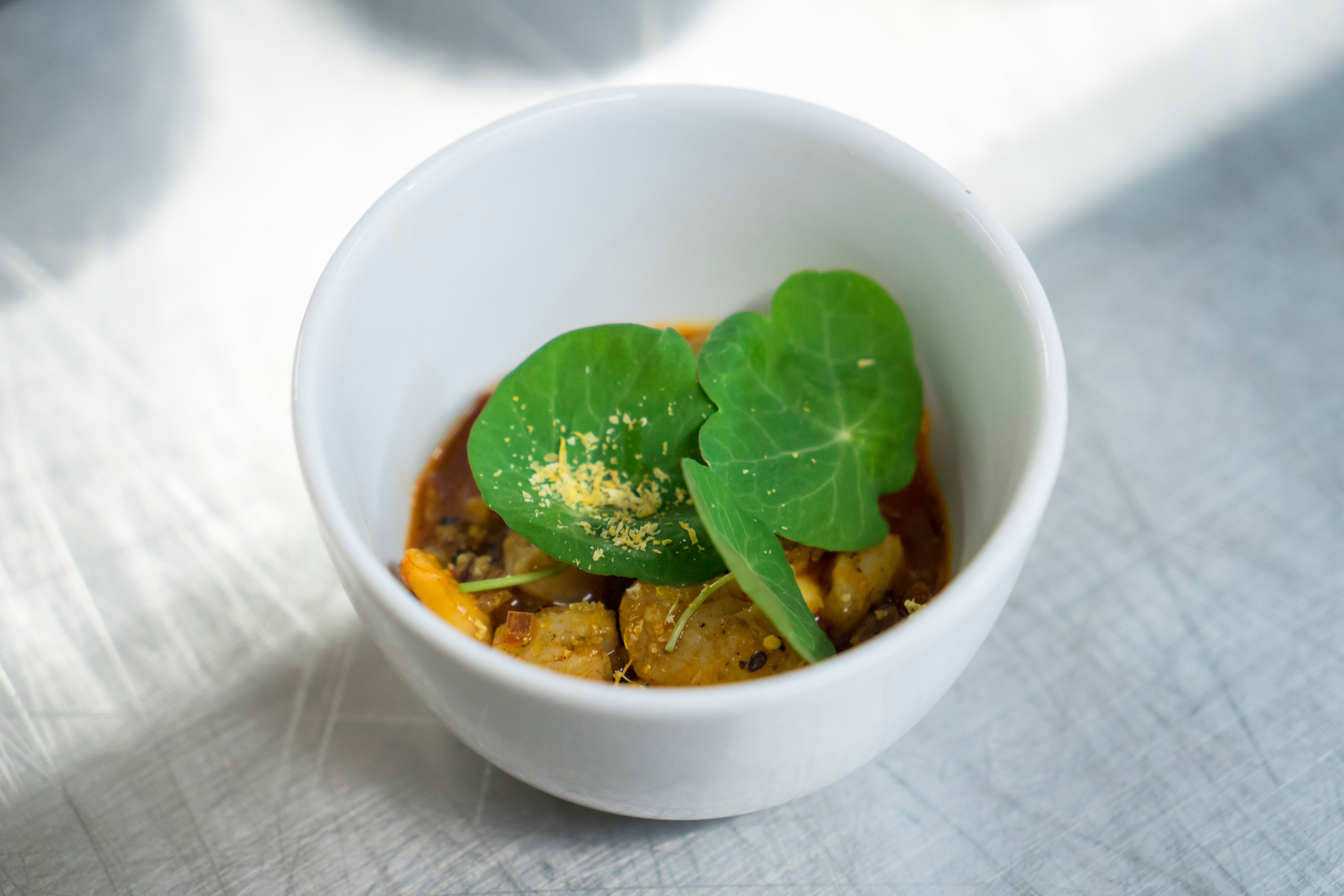 A single fine-dining course in a white bowl on a steel counter