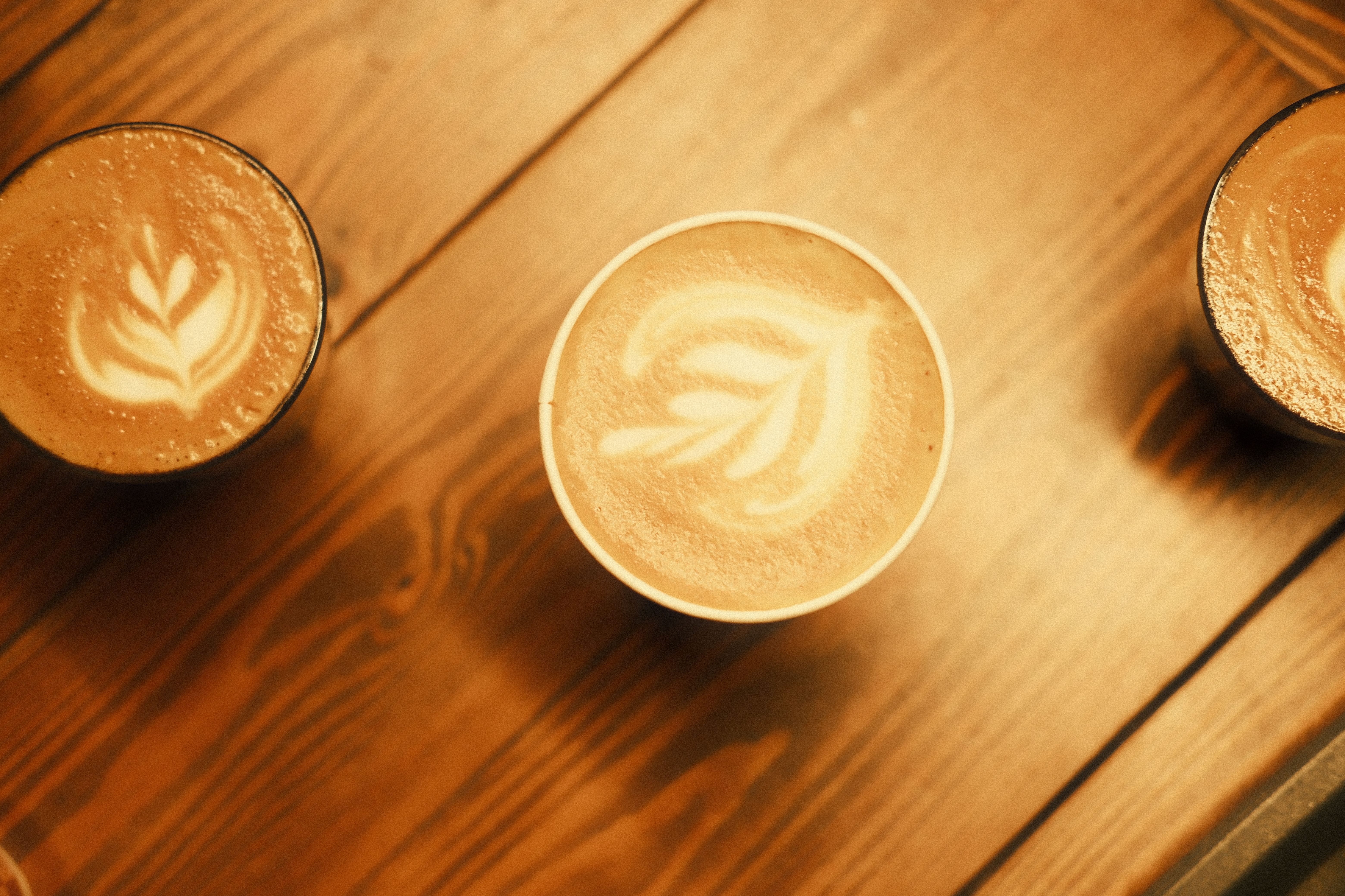 Latte art on three coffees seen from above on a wooden table