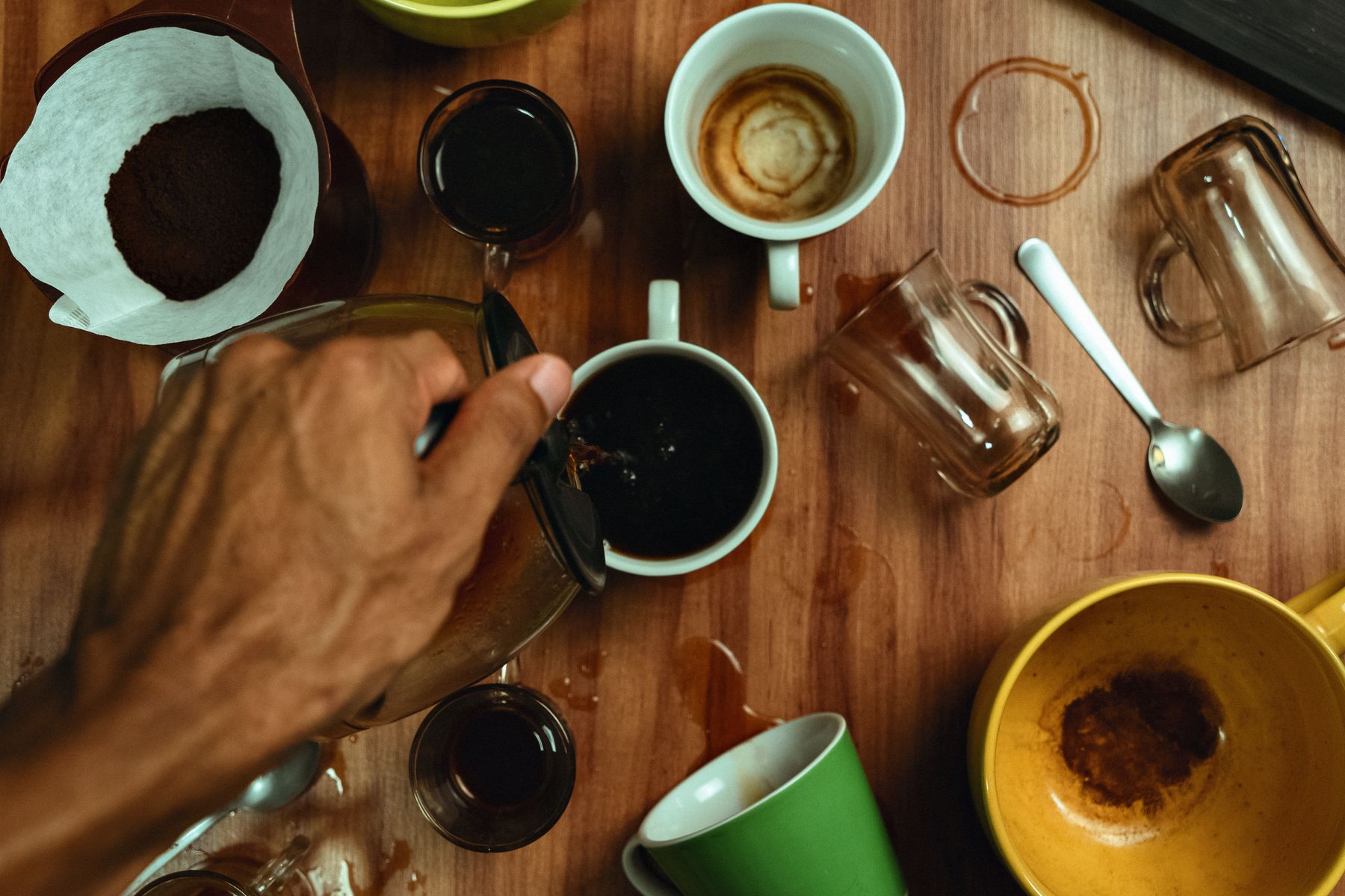 Eine Hand gießt Filterkaffee in eine Tasse zwischen mehreren Verkostungstassen auf einem Holztisch