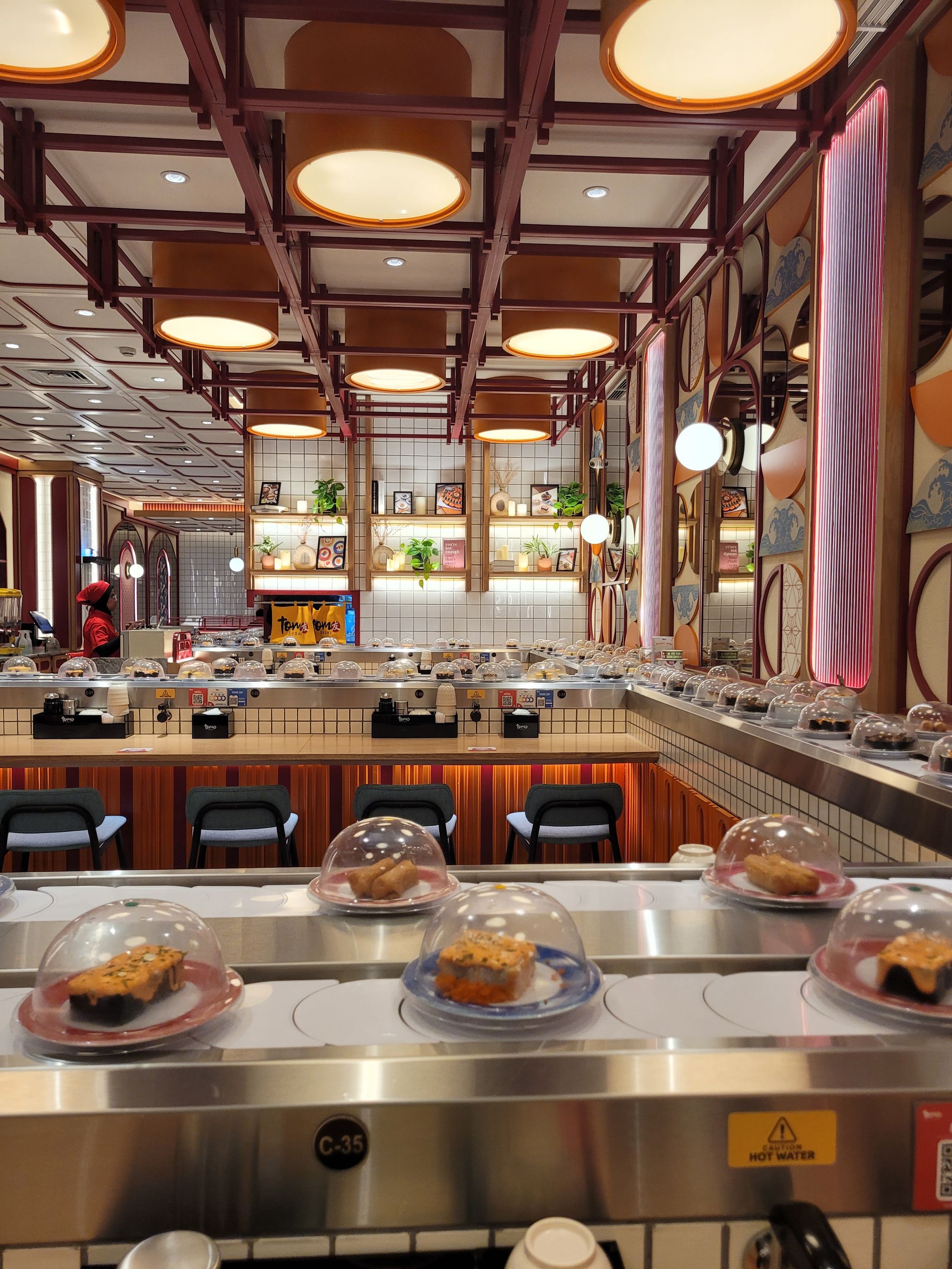 Intérieur d'un restaurant de sushis à tapis roulant avec assiettes couvertes et tabourets de bar