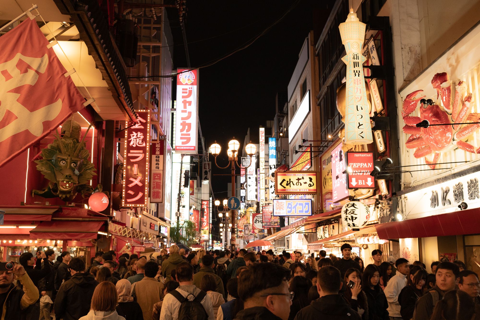 Belebte Dotonbori-Straße in Osaka bei Nacht unter Neonschildern für Ramen, Kushikatsu und Krabben