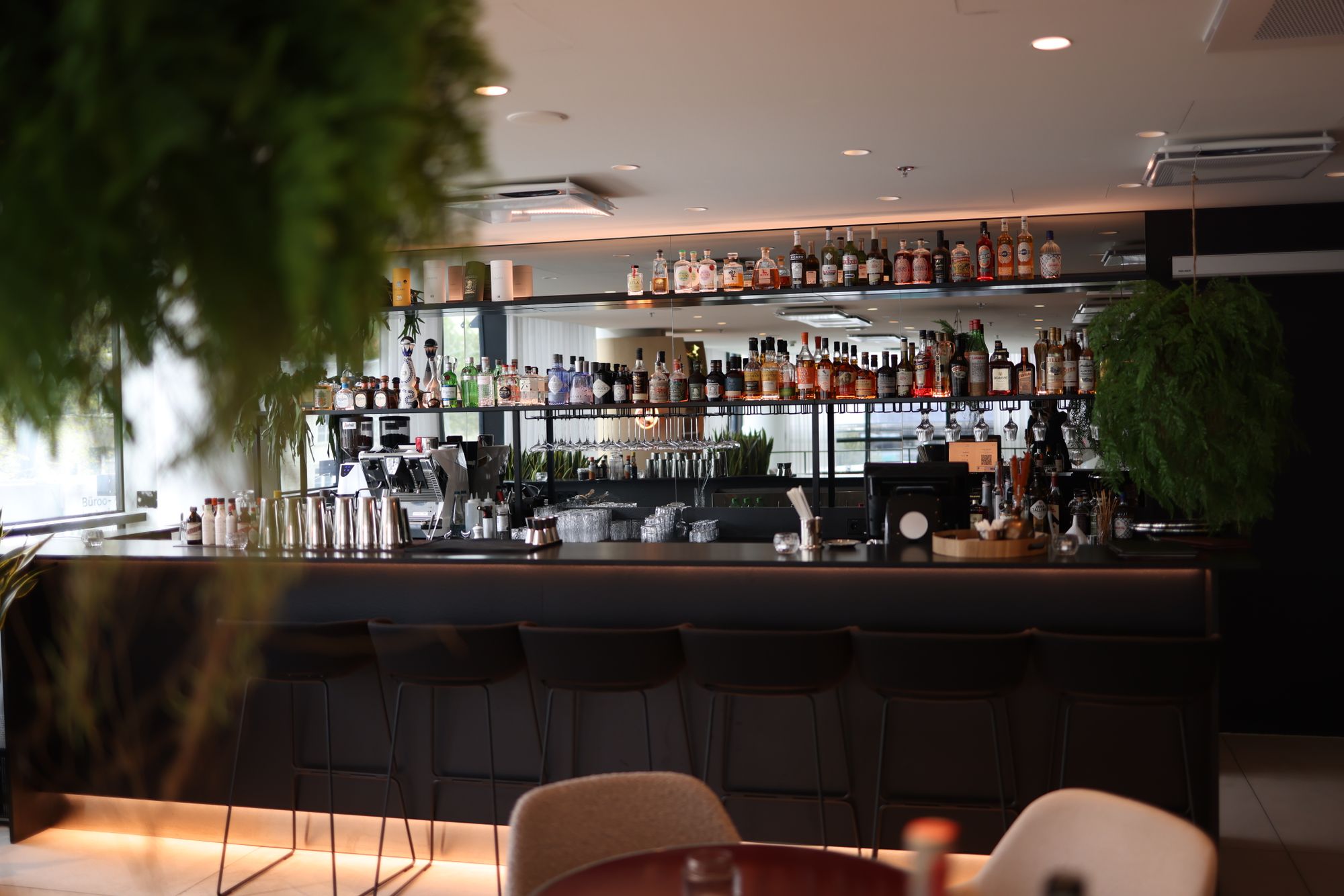 Bancone di un cocktail bar vuoto con sgabelli e una parete di bottiglie, illuminato e senza personale