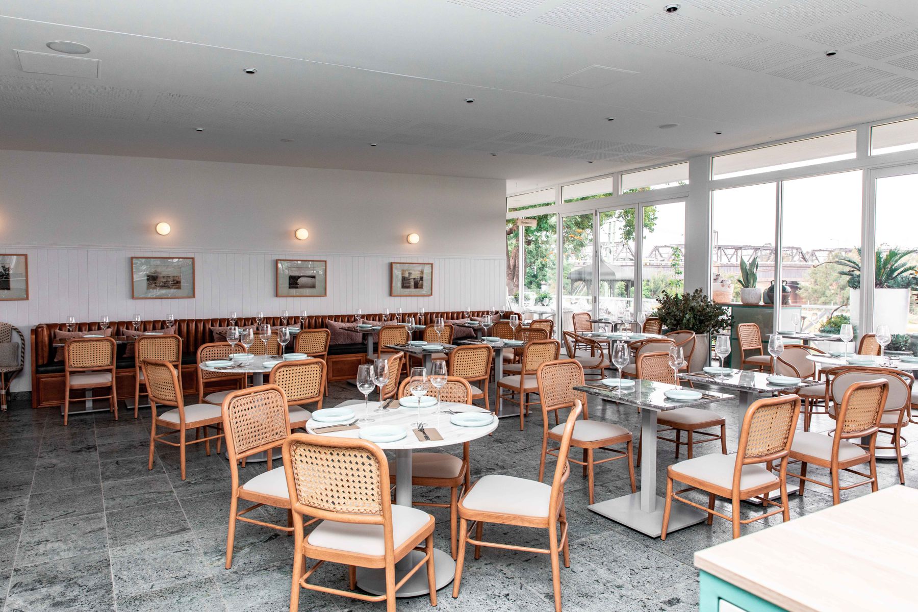 Sala di ristorante vuota con tavoli apparecchiati, sedie in paglia e grandi finestre