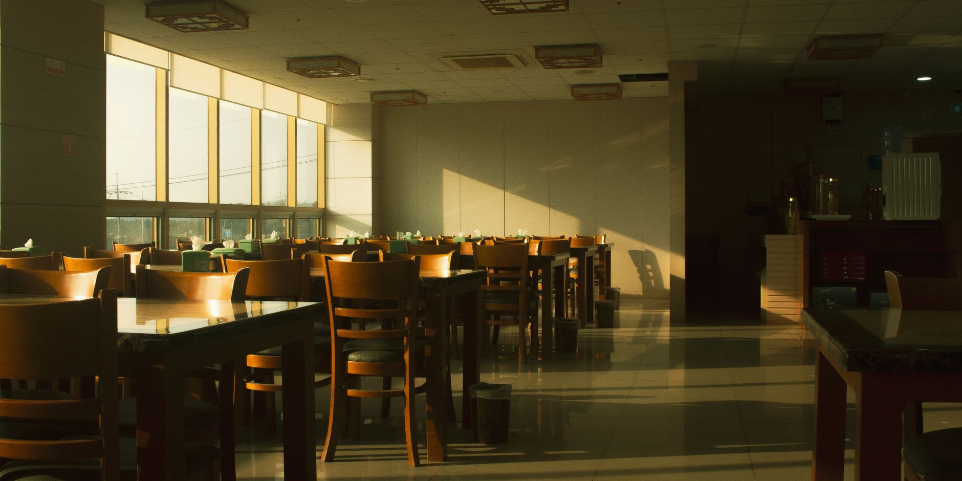 Comedor de restaurante vacío iluminado por el sol con mesas y sillas de madera