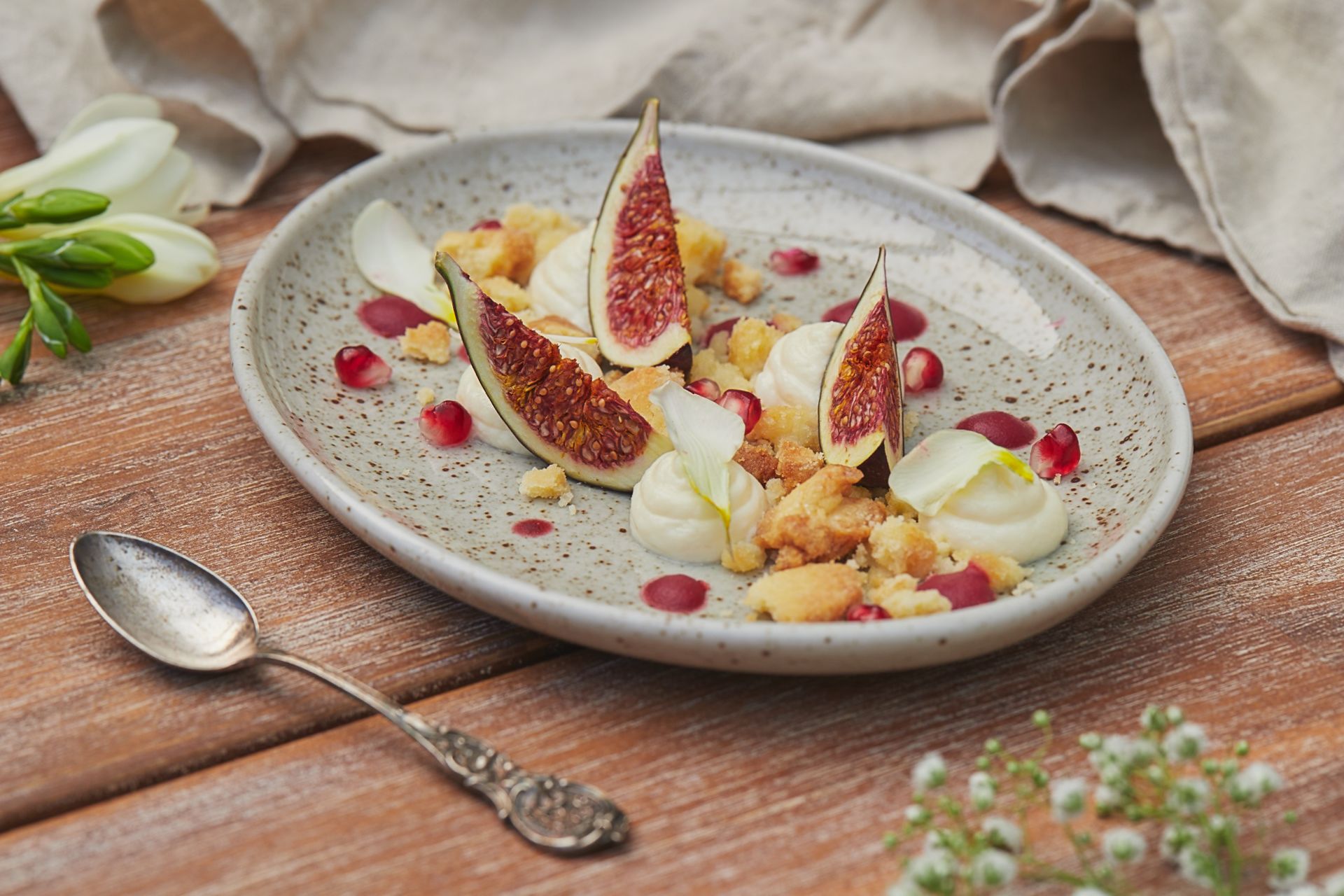 Fig wedges with cream, crumble and pomegranate seeds on a speckled plate