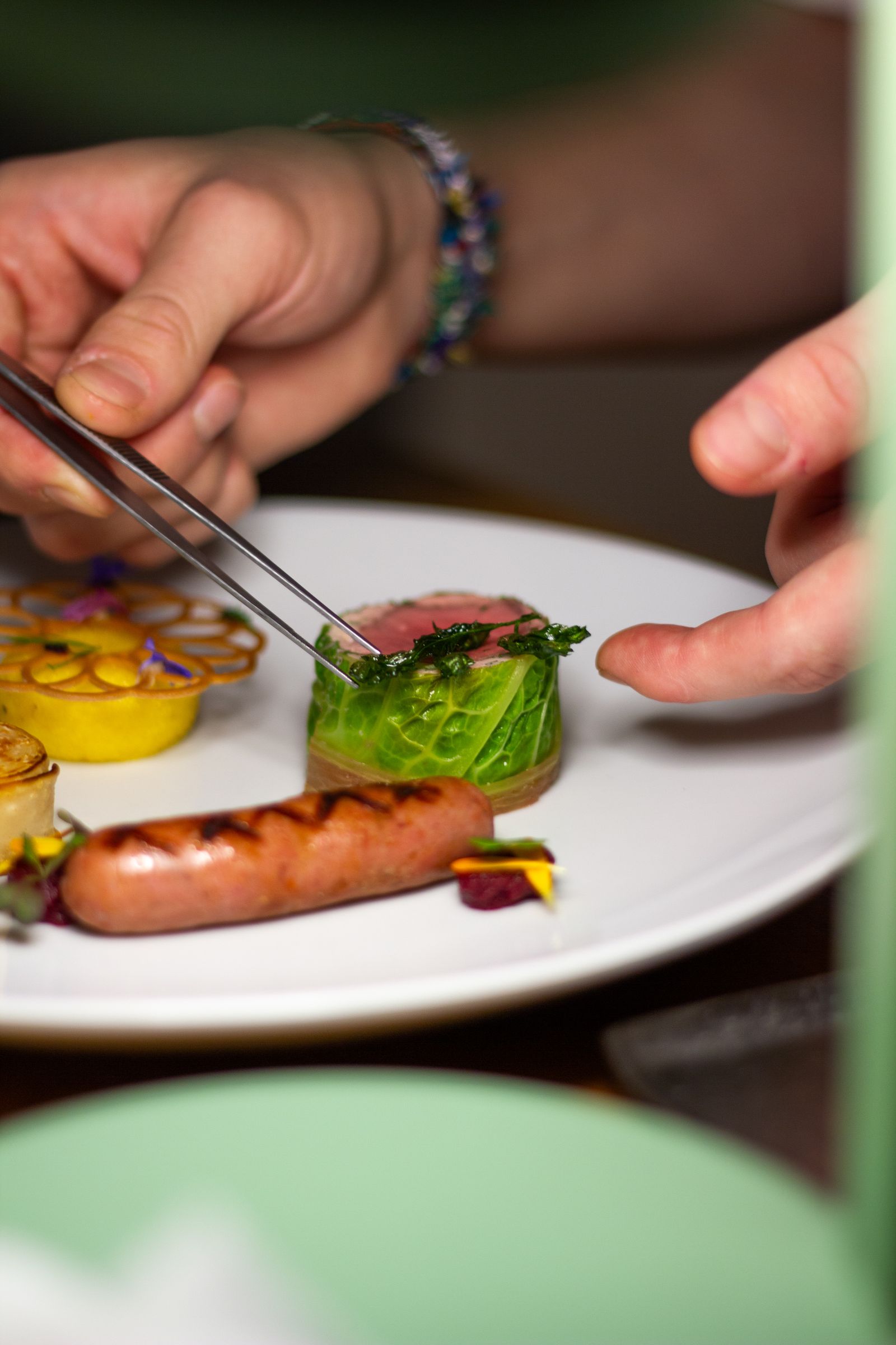 Chef's hands using tweezers to garnish a fine dining plate with herbs