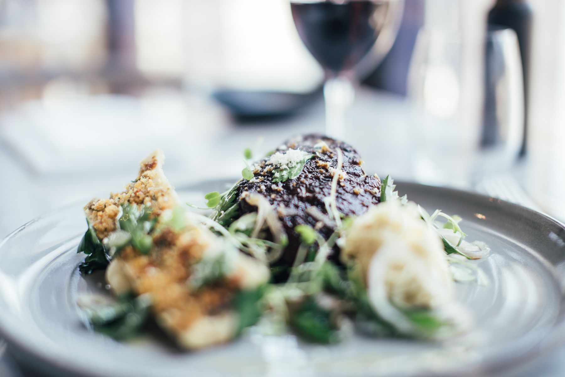 A plated dish with meat and greens on a table in a contemporary restaurant dining room