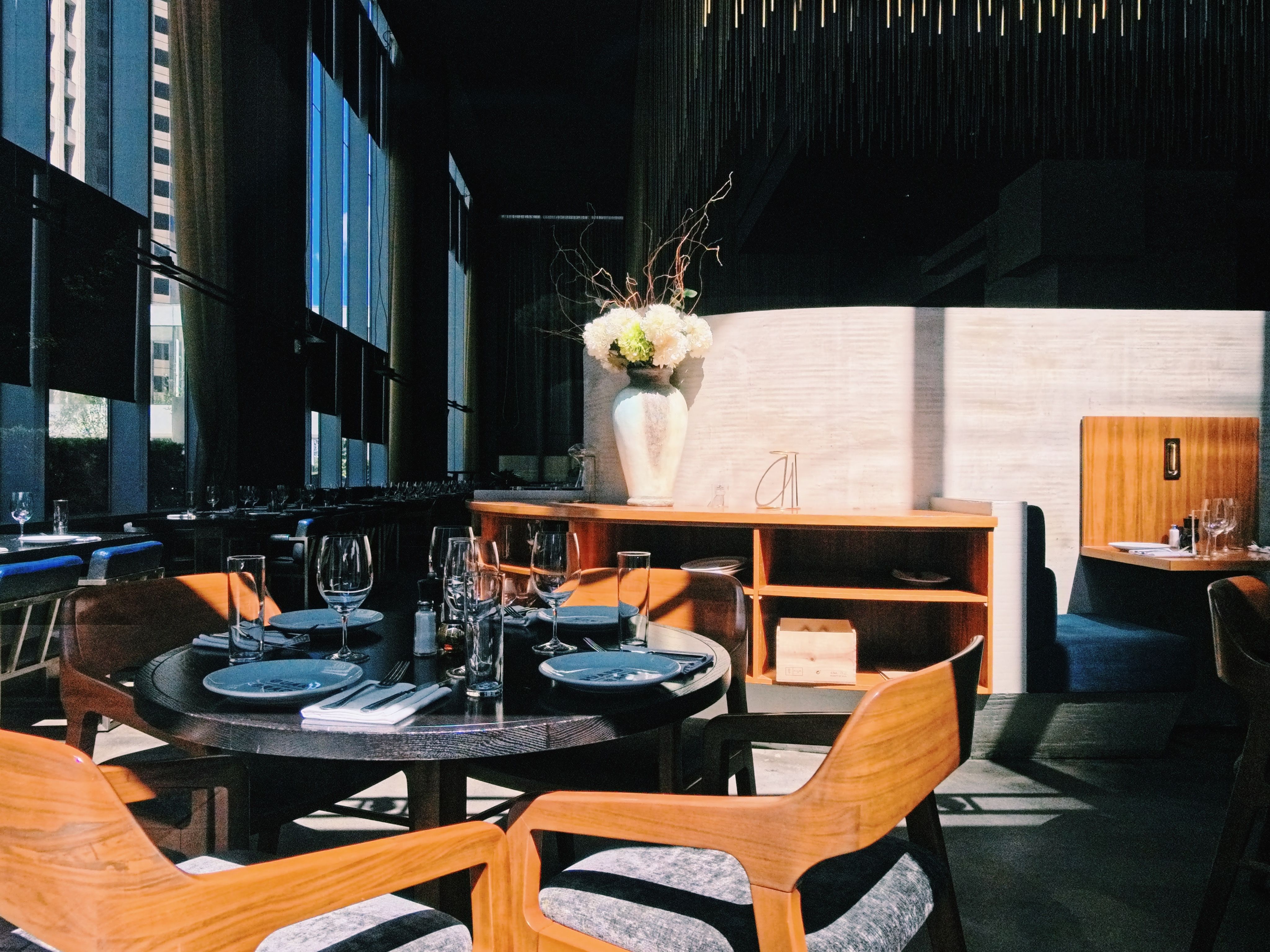 A dimly lit modern restaurant dining room with a set table and wine glasses