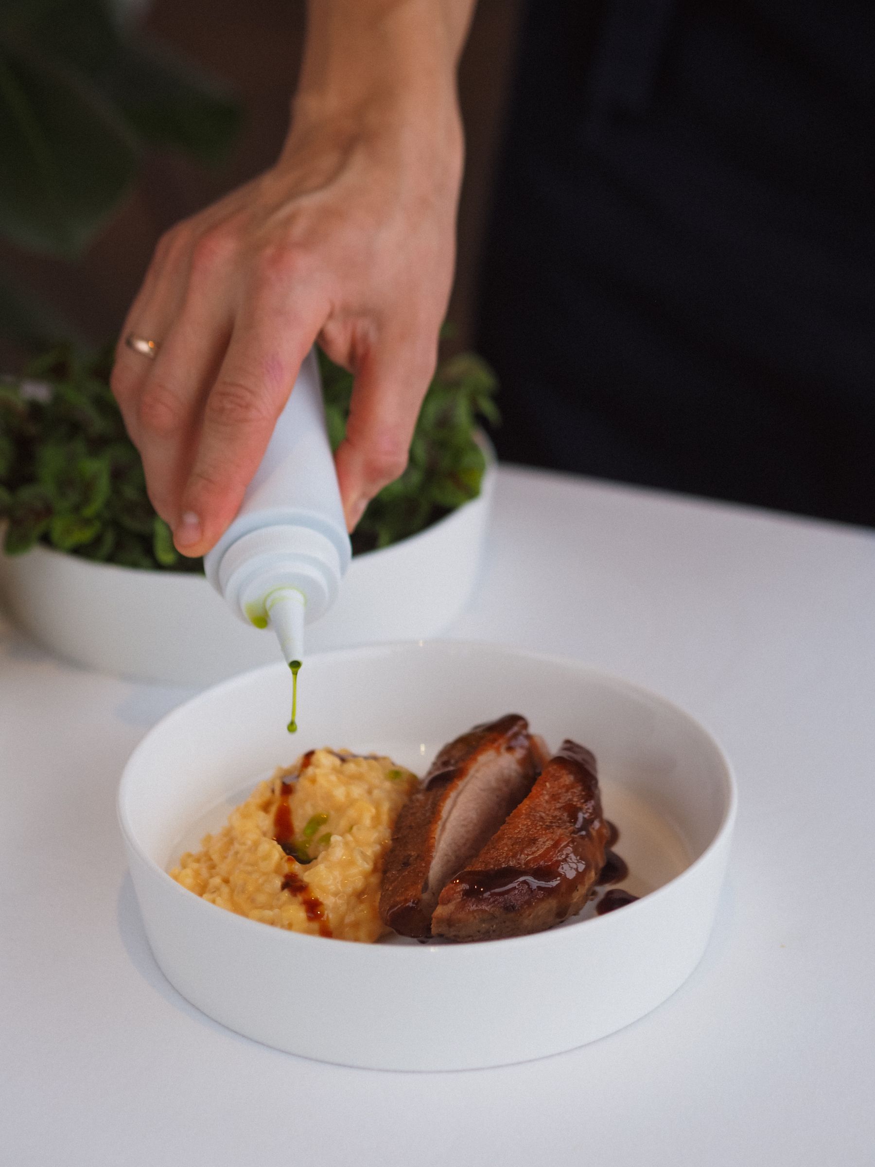 A chef's hand finishing a fine-dining plate with a sauce drizzle