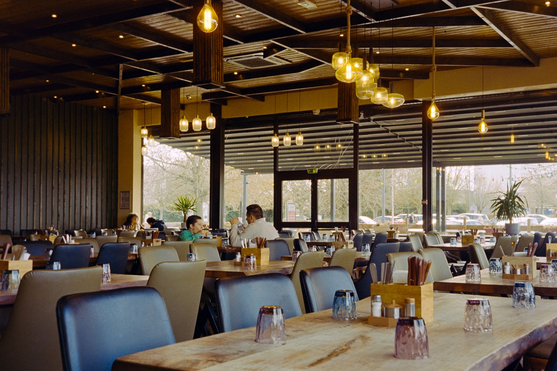 Gäste an Holztischen in einem warm beleuchteten Bistro-Speisesaal