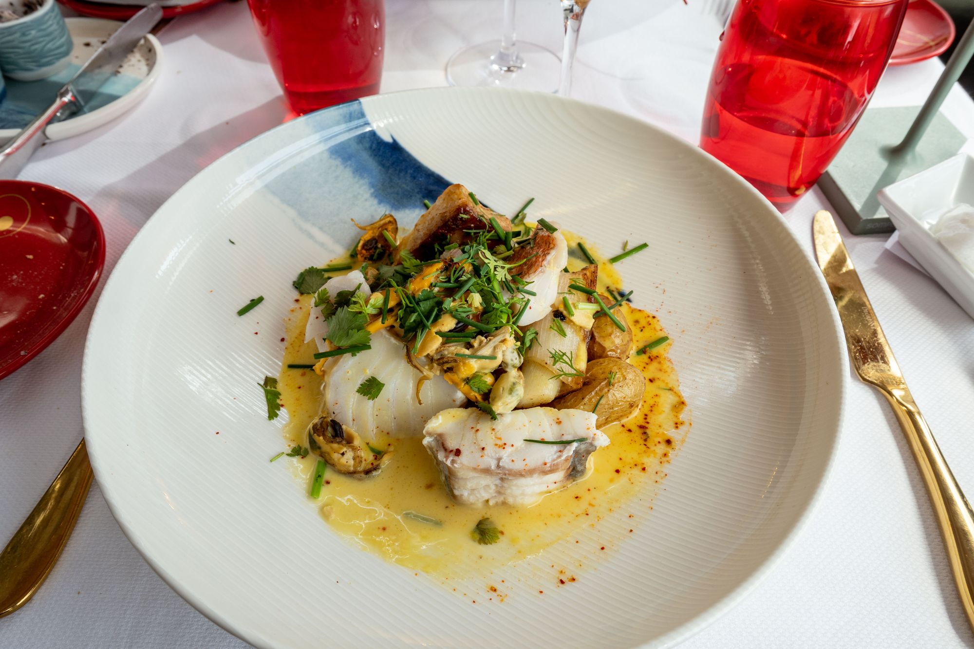 Poisson dressé avec moules, pommes de terre et sauce au beurre dans une assiette creuse blanche sur une table dressée