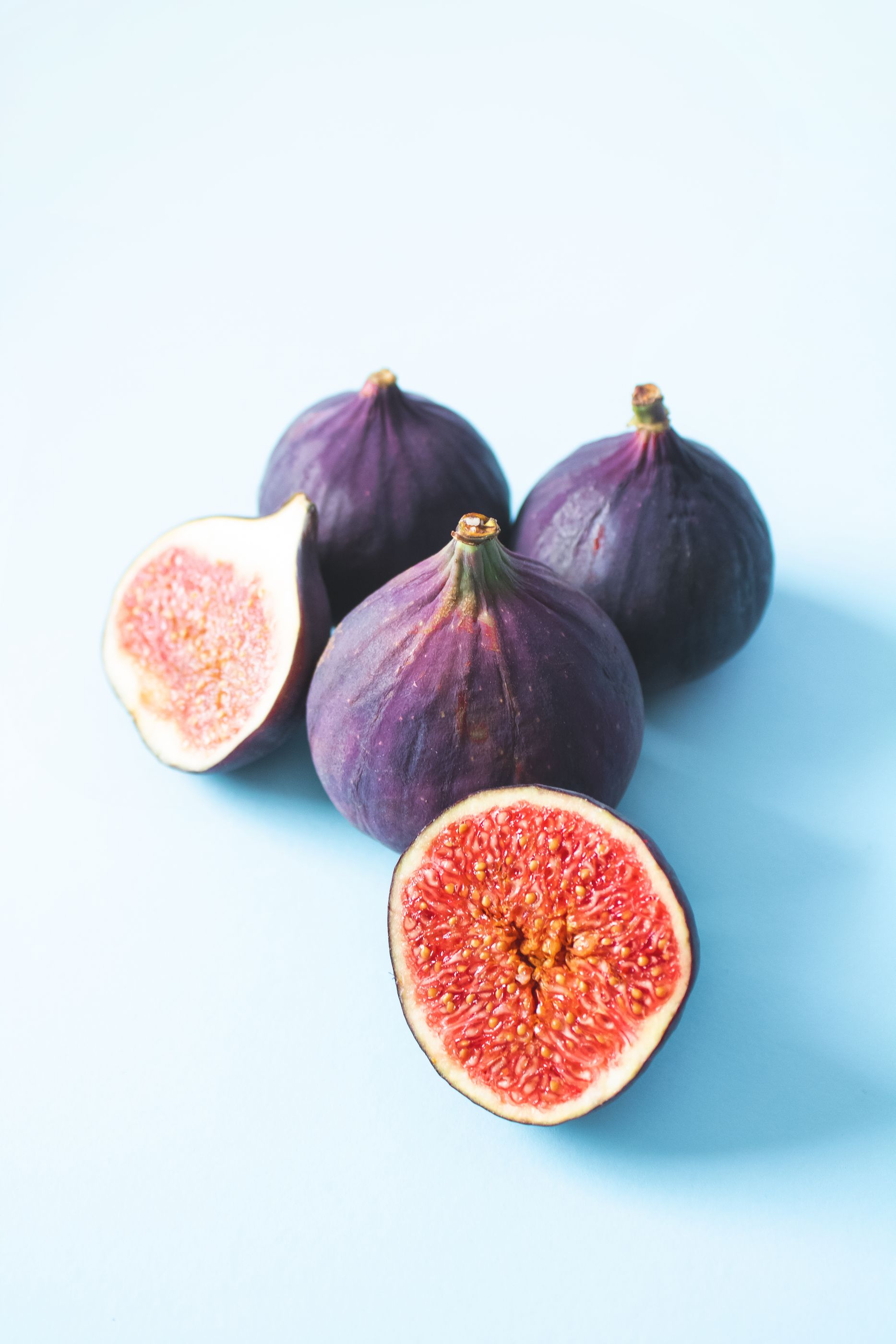 Figues violettes fraîches entières et coupées en deux montrant leur chair rouge sur un fond bleu pâle