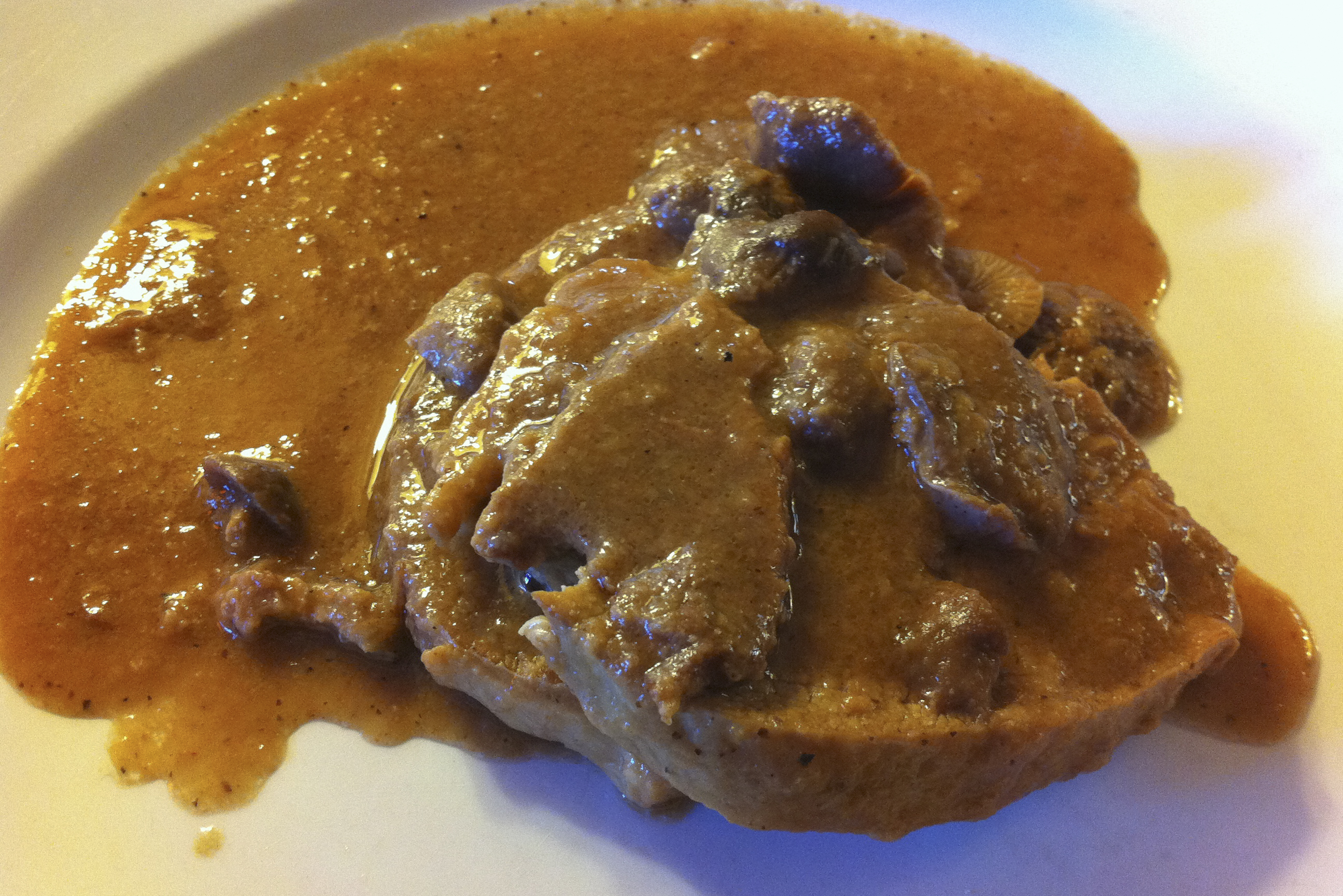 Veal fricandó with small wild mushrooms in a thick brown sauce on a white plate