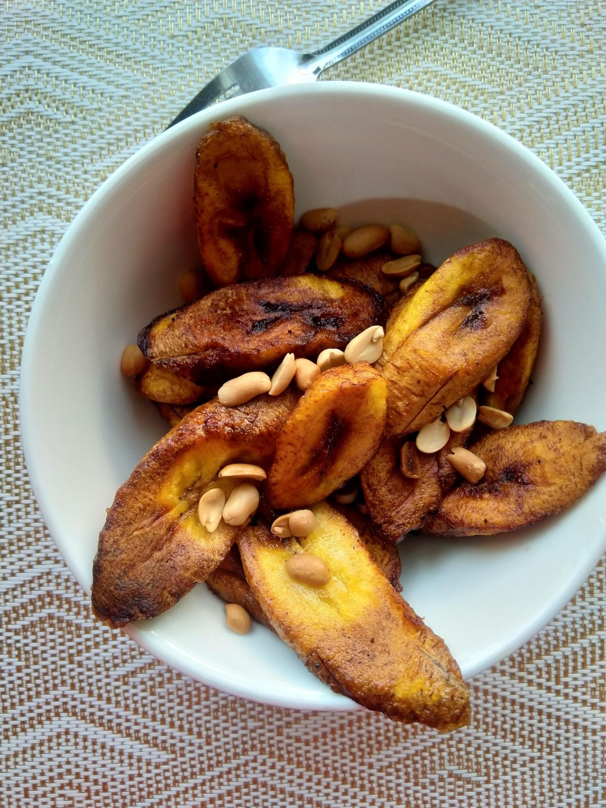 A bowl of golden fried plantain slices topped with roasted peanuts