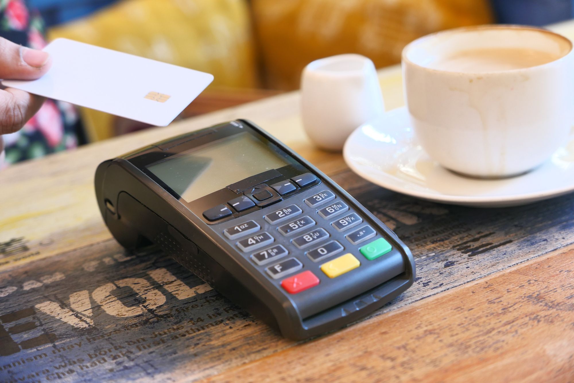 Card payment terminal on a wooden café table next to a cup of coffee