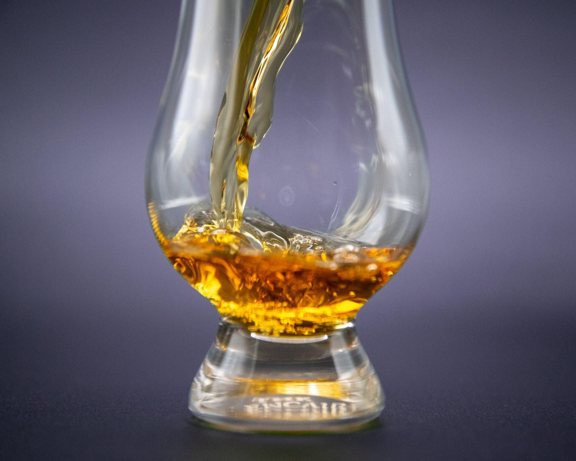 Amber whisky being poured into a Glencairn tasting glass against a dark background