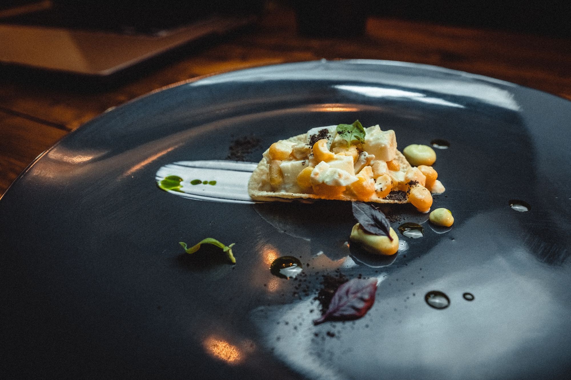 Tasting-menu course plated on a dark ceramic plate under low restaurant light
