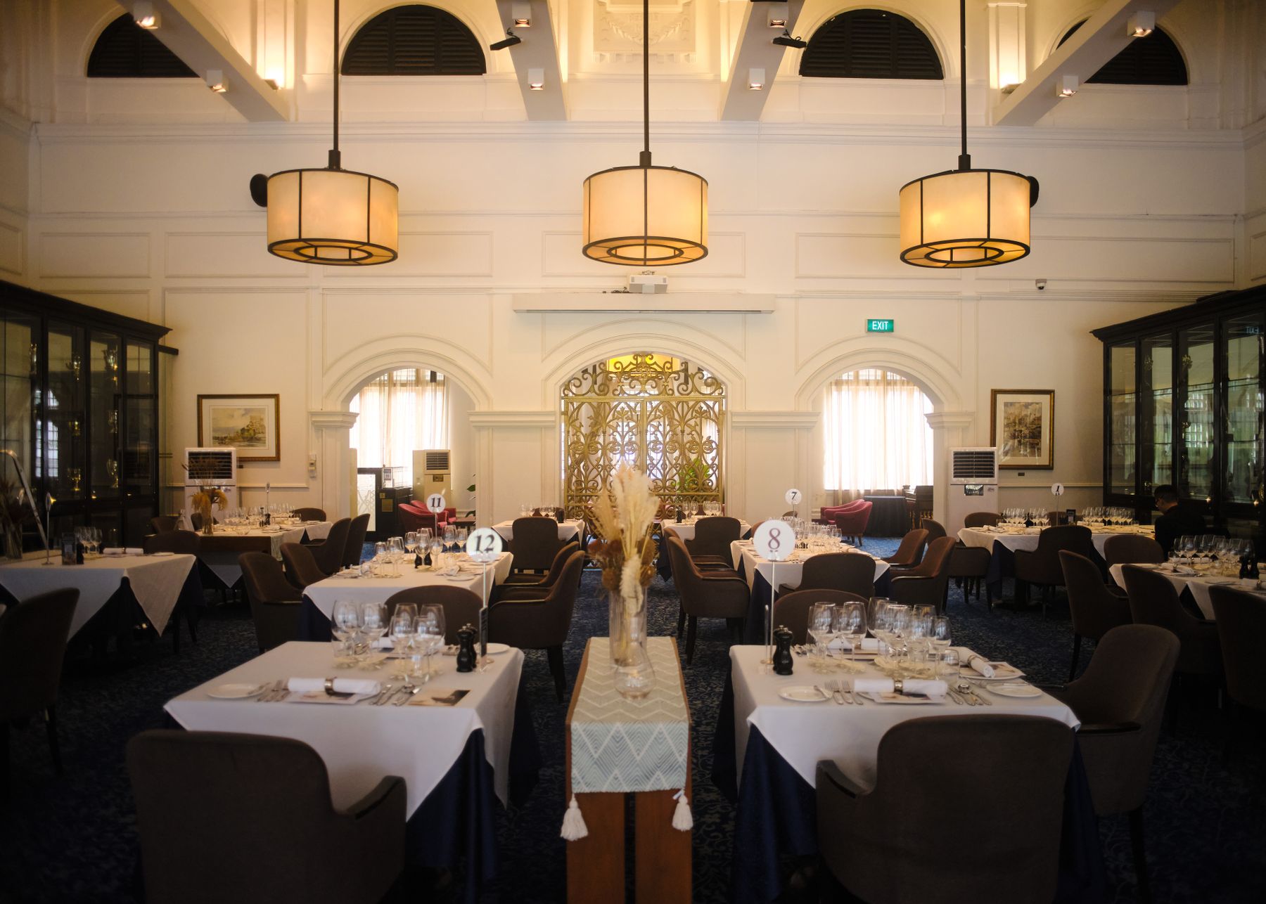 A colonial-style dining room with arched windows, drum pendant lights and a gilded screen