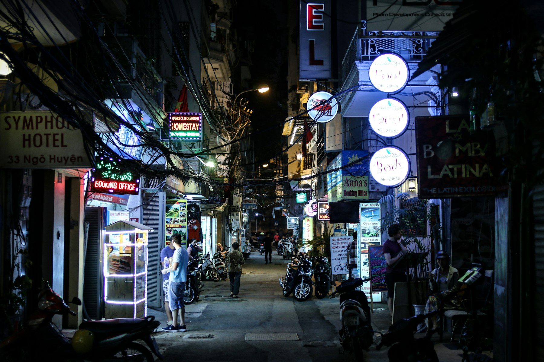 Carteles de neón y cables enredados sobre una calle estrecha del Casco Antiguo de Hanói de noche