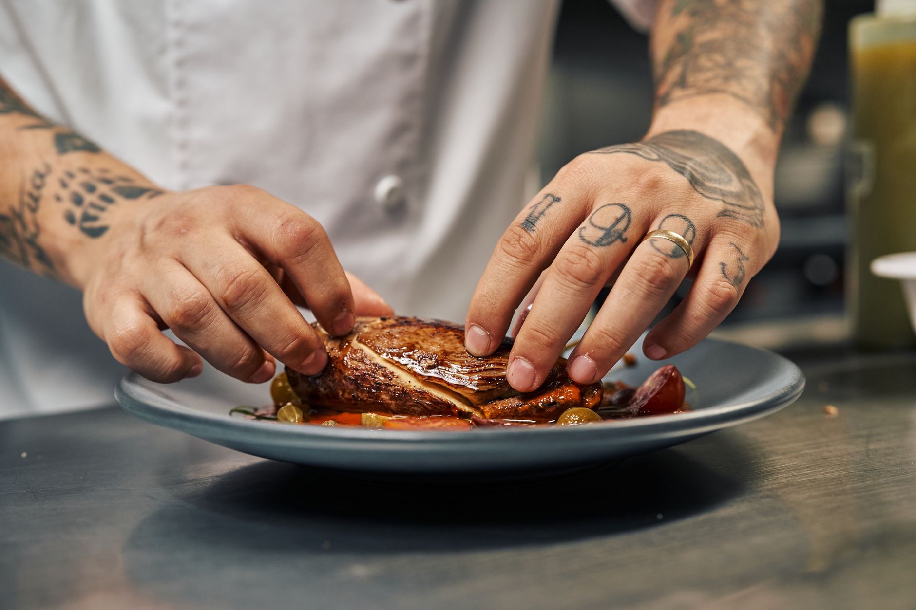 A chef's hands plating a seared dish in a professional kitchen