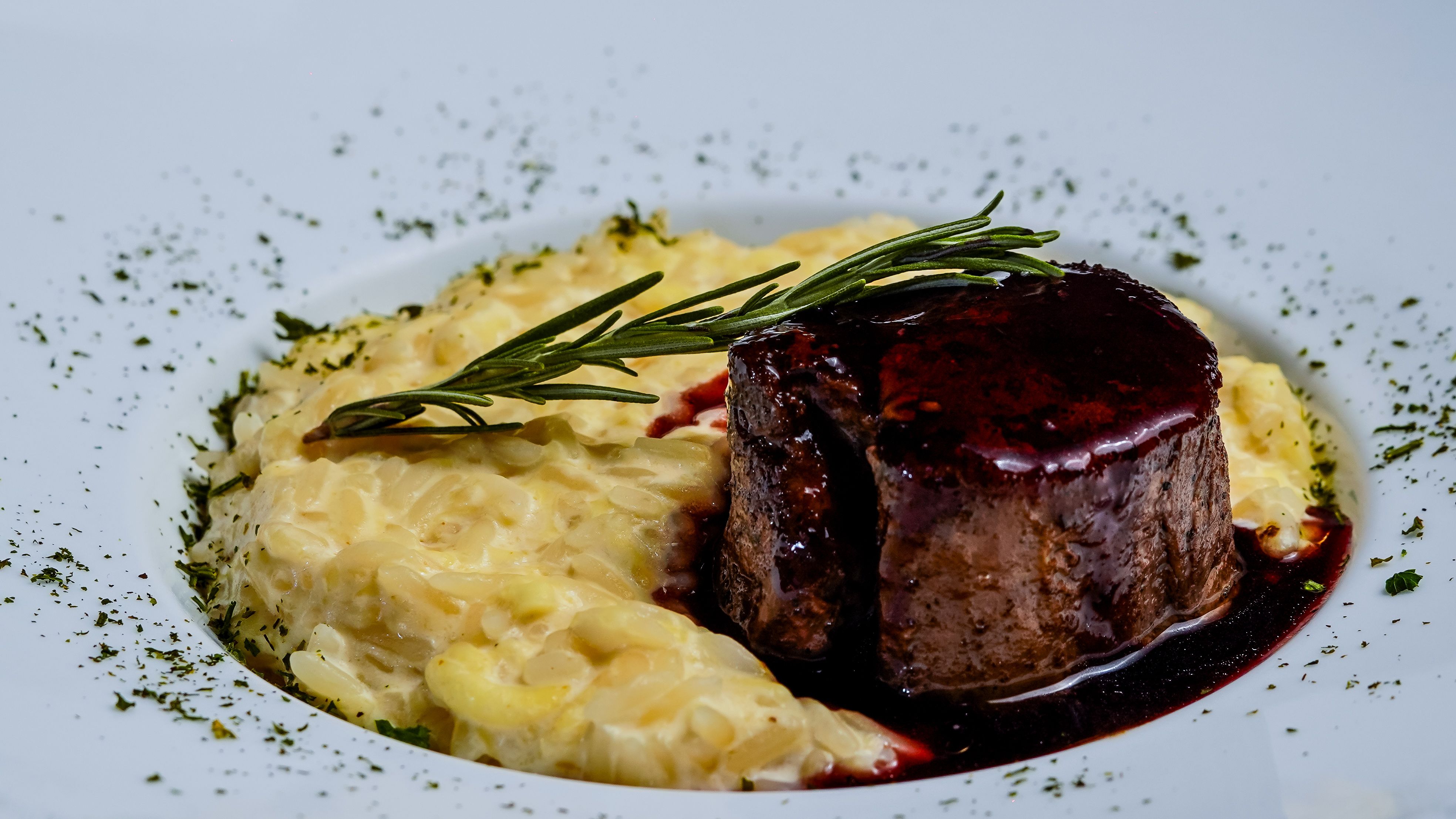 Seared filet mignon in red wine sauce with rosemary sprig on creamy risotto