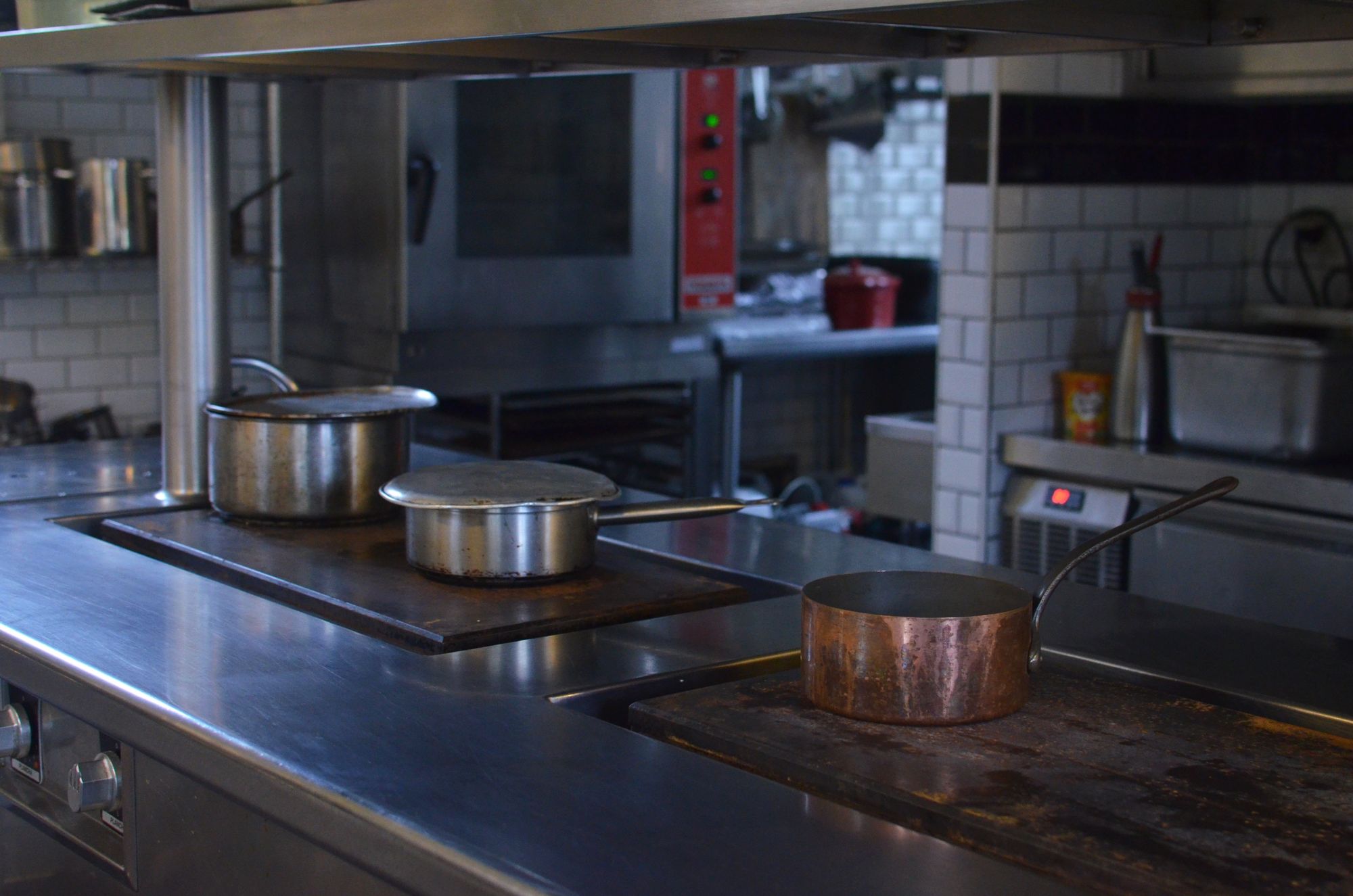 Copper and steel pans on the stove of an empty professional restaurant kitchen