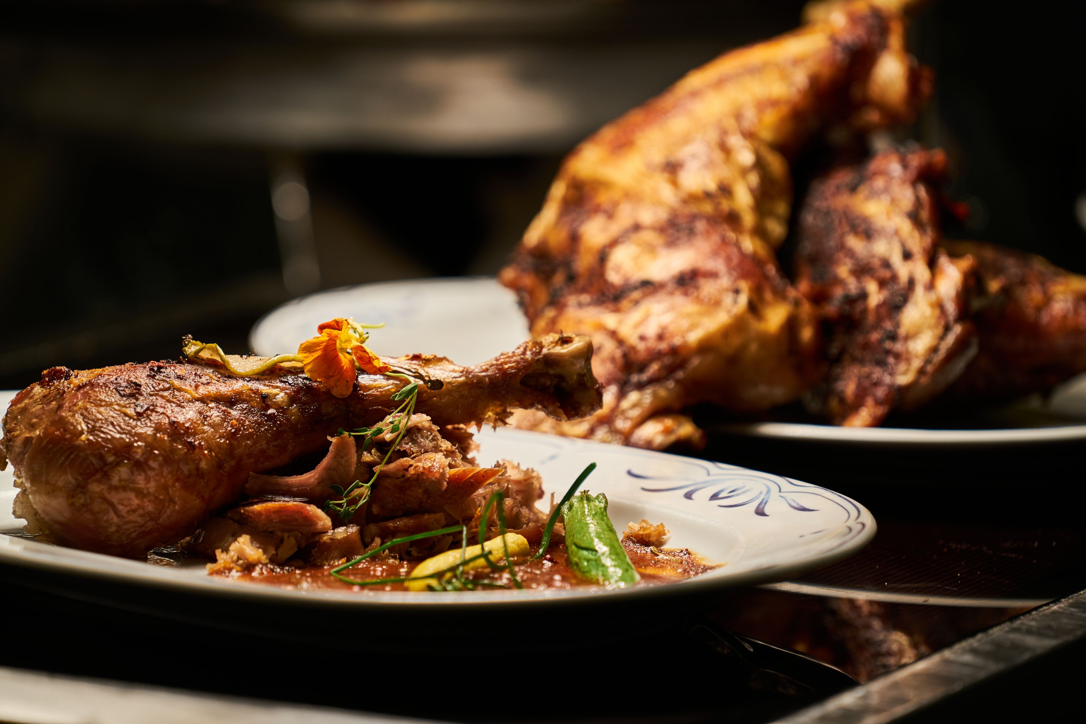 Roast chicken leg plated elegantly with herbs and a flower garnish, fine-dining style