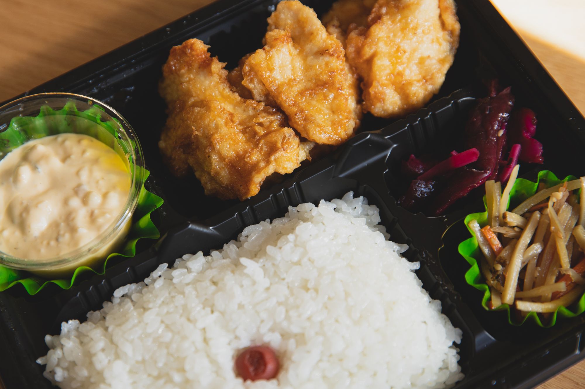Bento zum Mitnehmen in schwarzer Plastikschale mit frittiertem Hähnchen, Reis und Eingelegtem