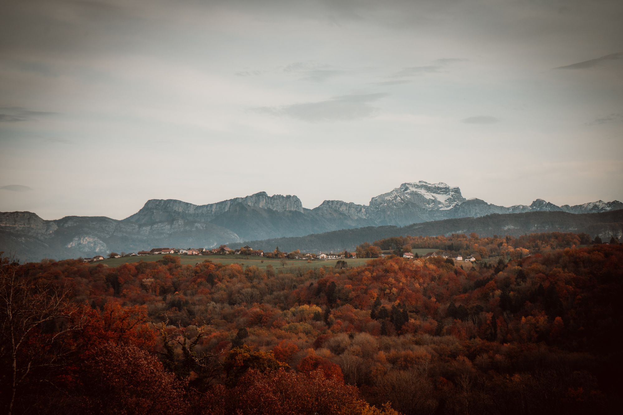 Autumn woodland and scattered hamlets below a grey limestone ridge