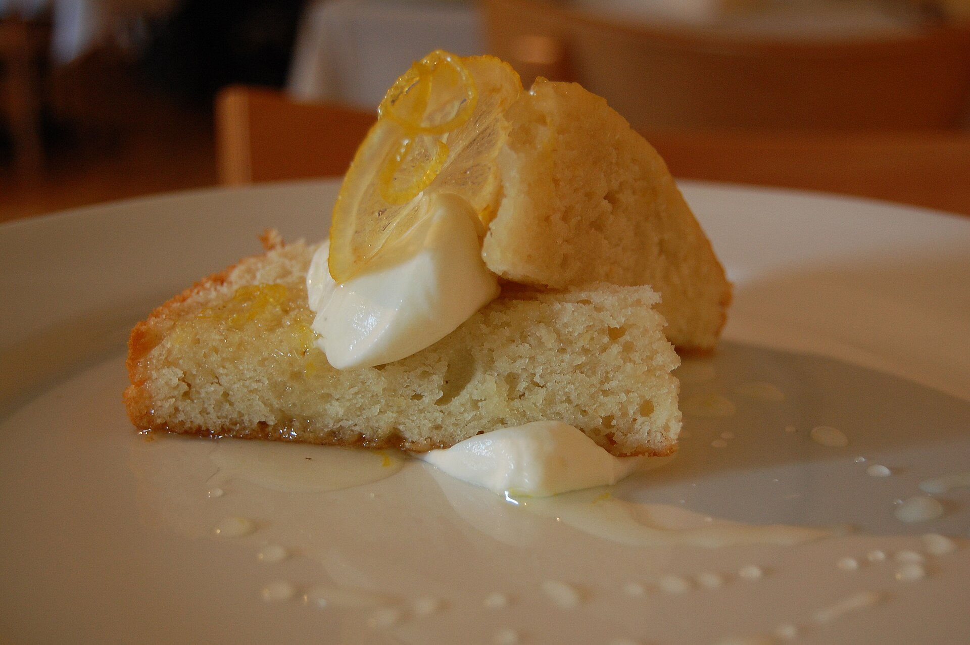 Wedge of lemon olive oil cake with cream and a candied lemon slice on a white plate