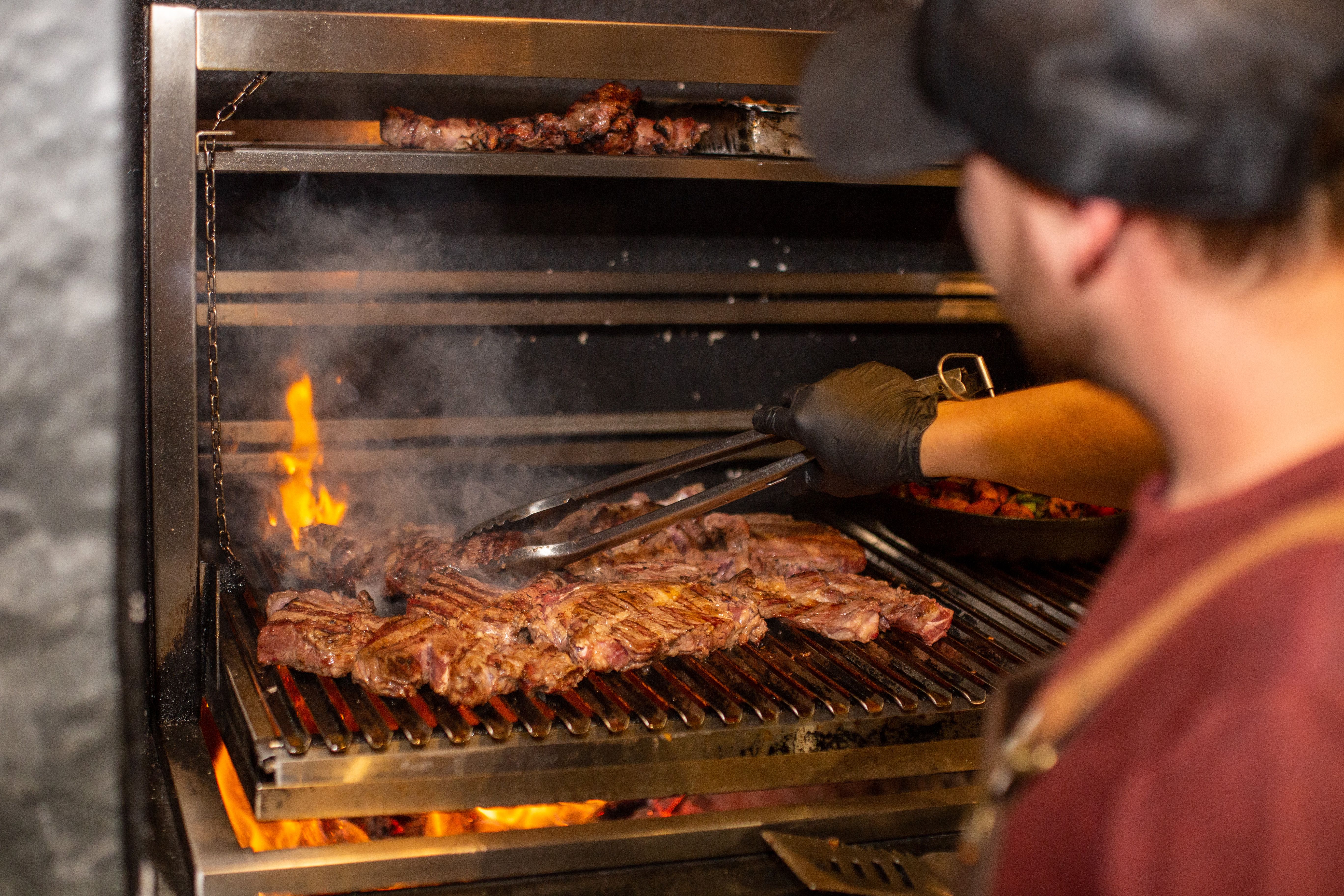 Chef grilling steaks over an open flame in a professional kitchen