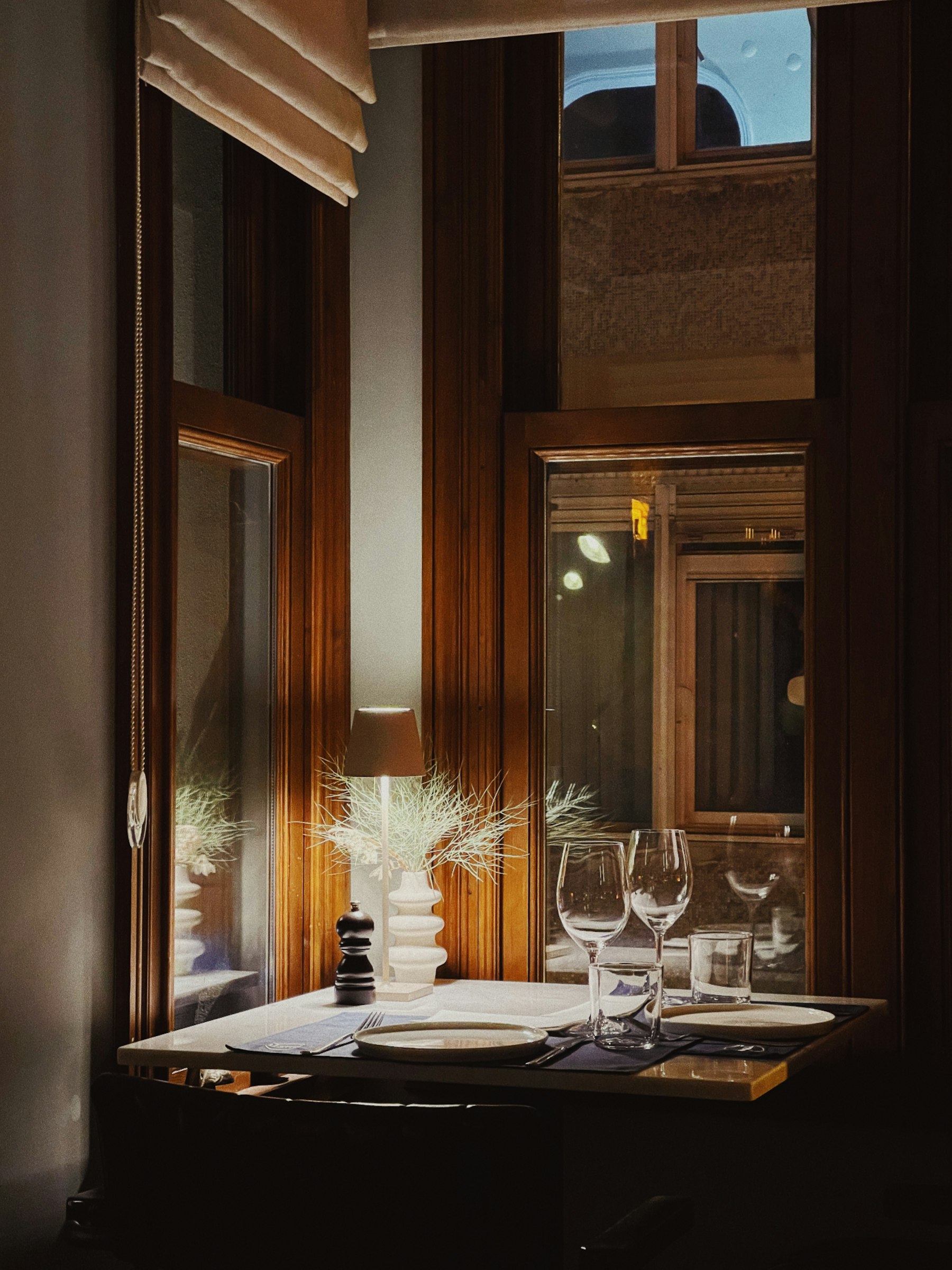 Een elegant gedekte restauranttafel met wijnglazen naast een hoog raam