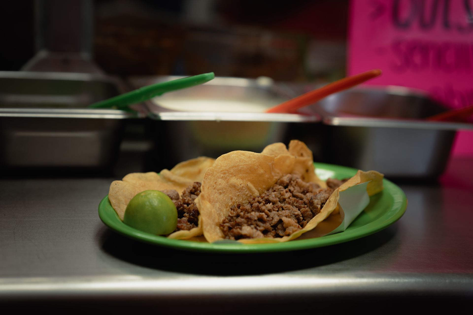Two beef tacos and a lime wedge on a green plate at a taqueria counter
