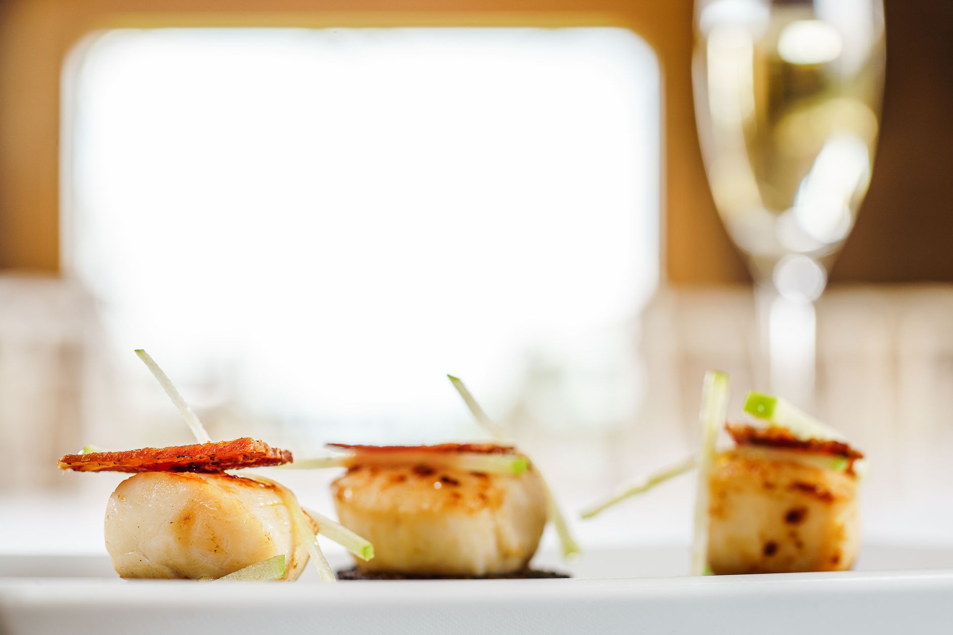 Coquilles Saint-Jacques saisies dressées sur une assiette avec un verre de vin flou en arrière-plan